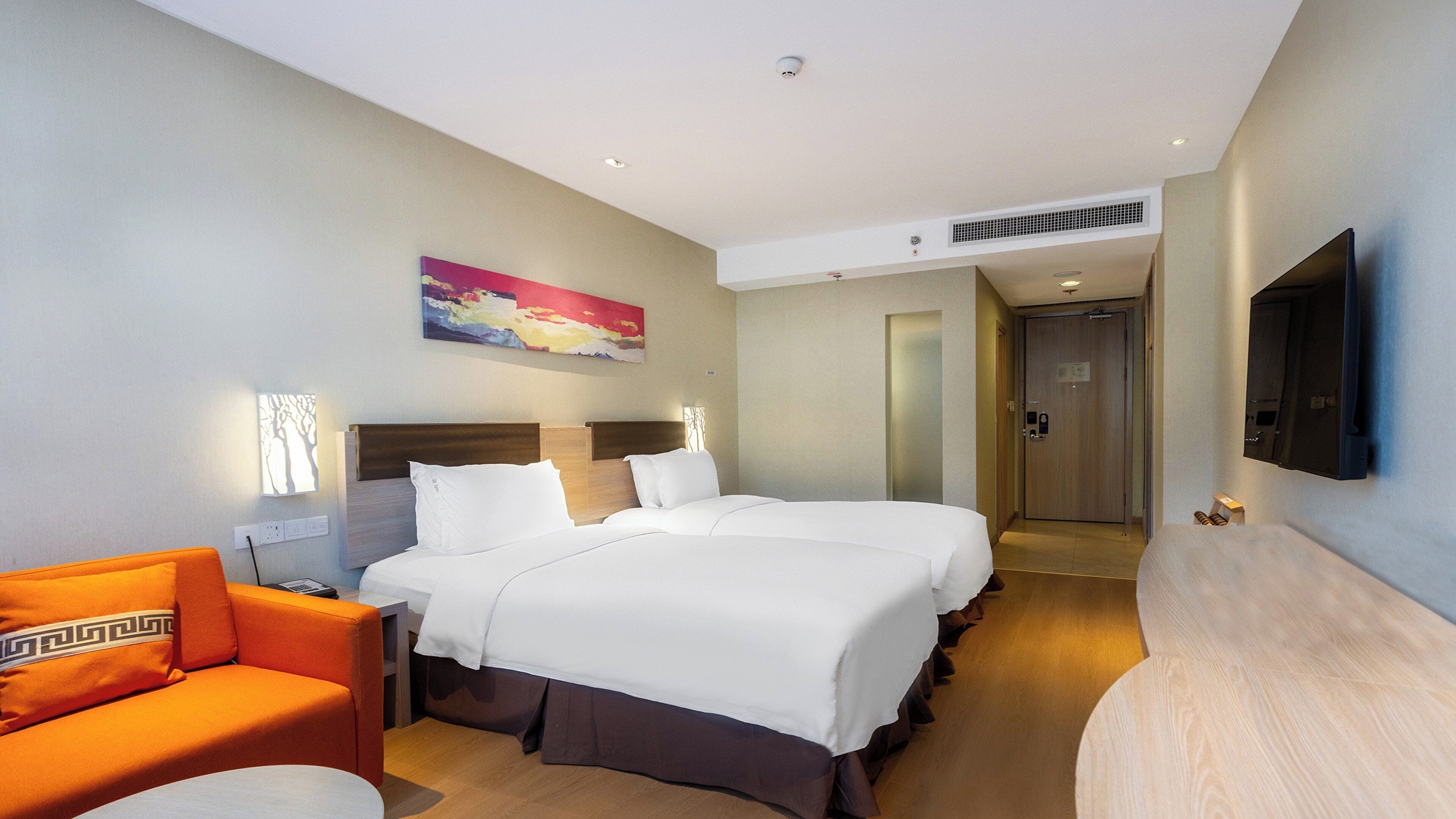 Una habitación de hotel con dos camas, un sofá, un televisor y un cuadro en la pared.