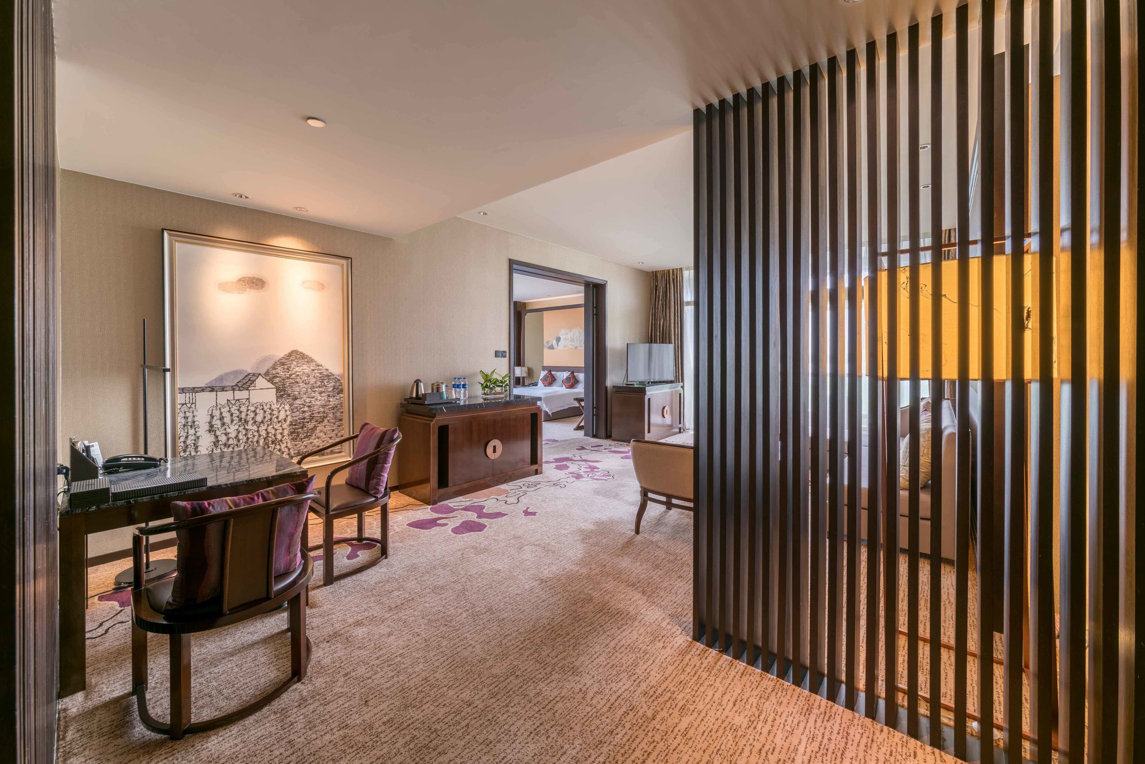 Ein Hotelzimmer mit Essbereich, Schreibtisch, Stuhl, Sofa, Lampe und einem großen Fenster.