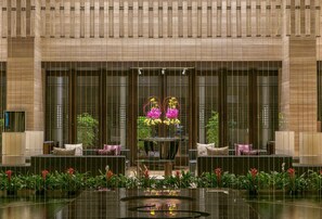 Un hall de hotel con zona de estar central, amplias ventanas y plantas de interior.