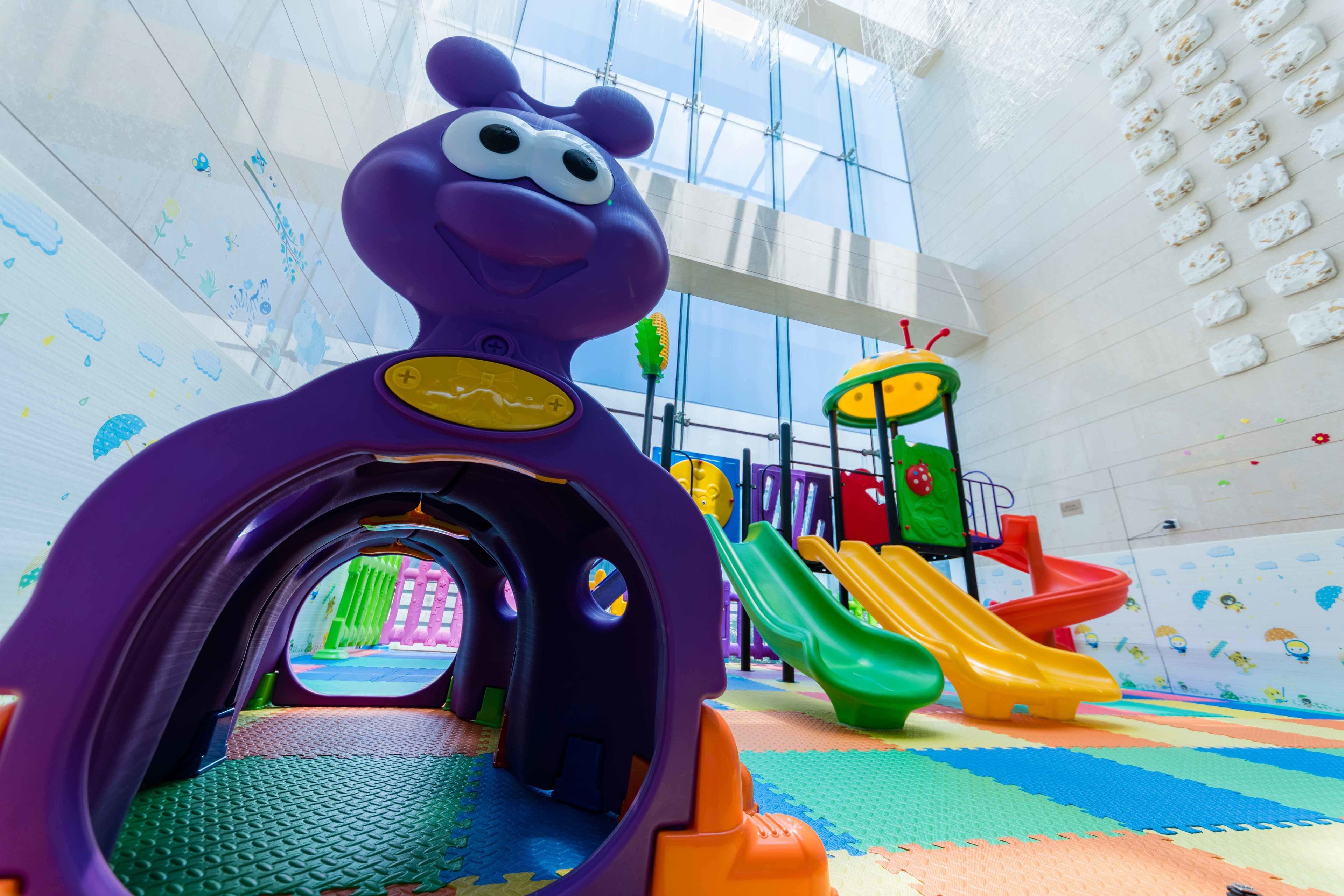 Ein Kinderspielbereich mit einem violetten Tunnel, Rutschen und einer Kletterkonstruktion.