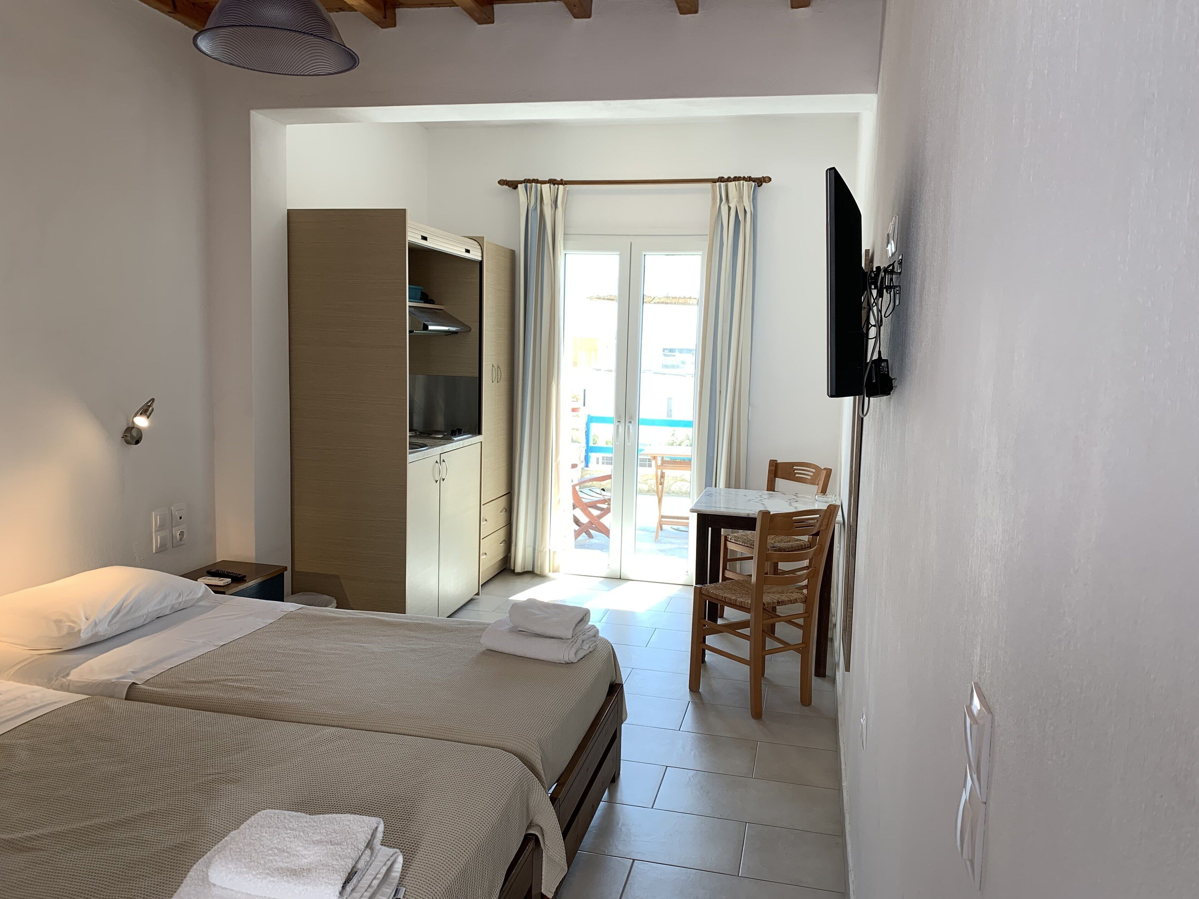 Un dormitorio con dos camas, una kitchenette, un comedor con mesa y sillas, y un televisor montado en la pared.