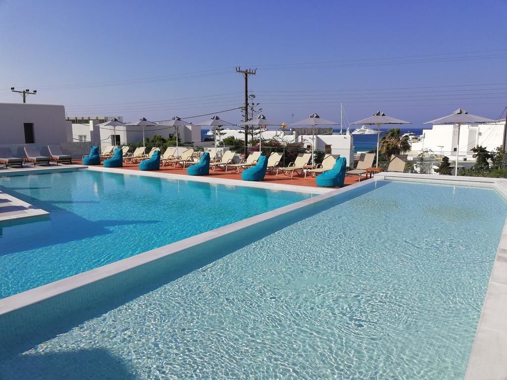 A swimming pool with lounge chairs and umbrellas, surrounded by white buildings and a clear sky.