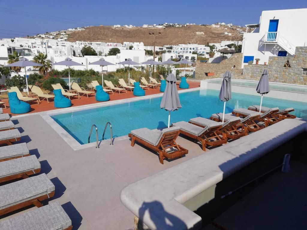 Un área junto a la piscina con sillones y sombrillas, vista despejada al mar y edificios blancos al fondo.