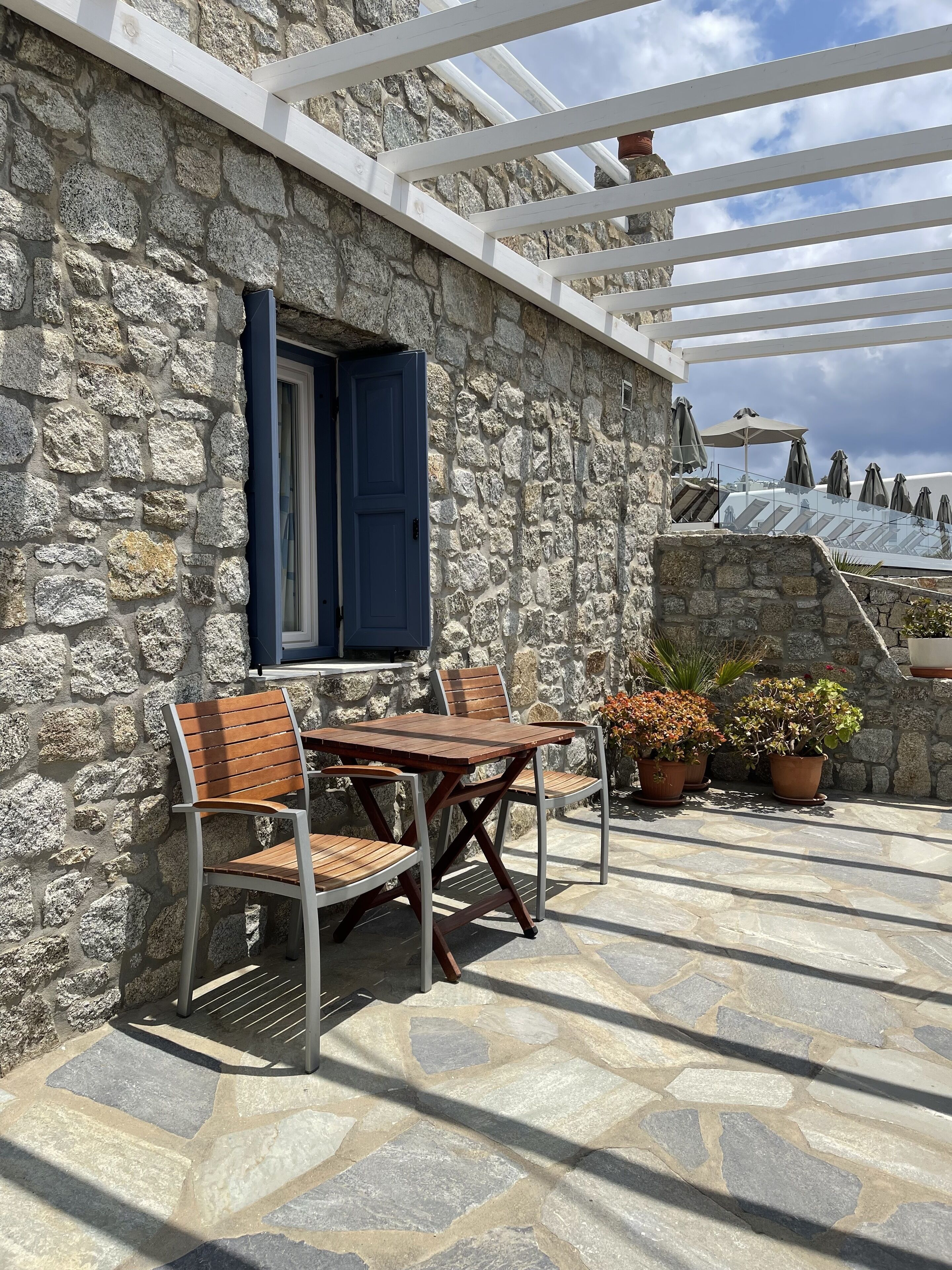 A stone building with a wooden table and chairs, a blue door, and potted plants.