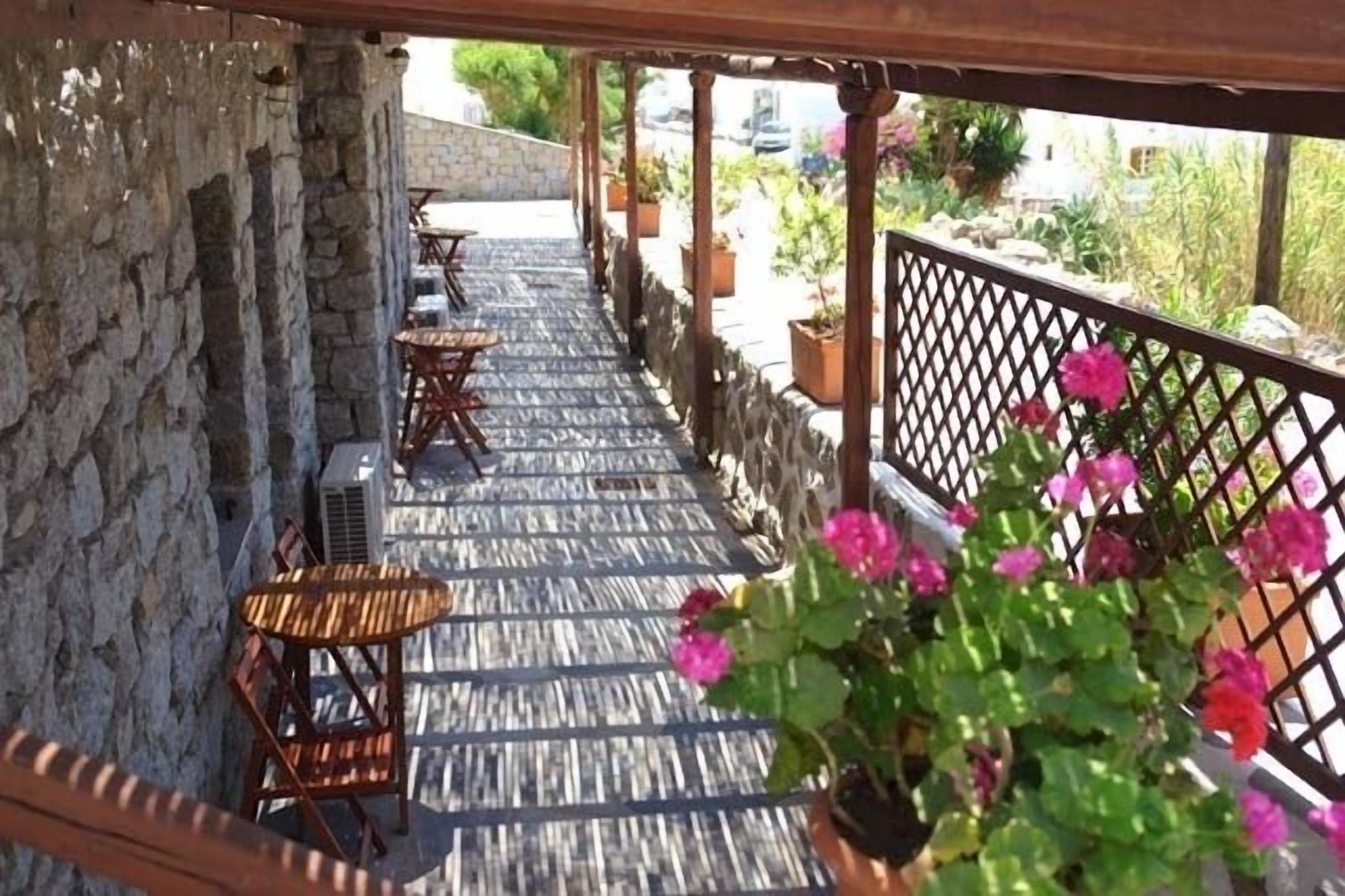 A covered outdoor seating area with stone walls and wooden tables and chairs.