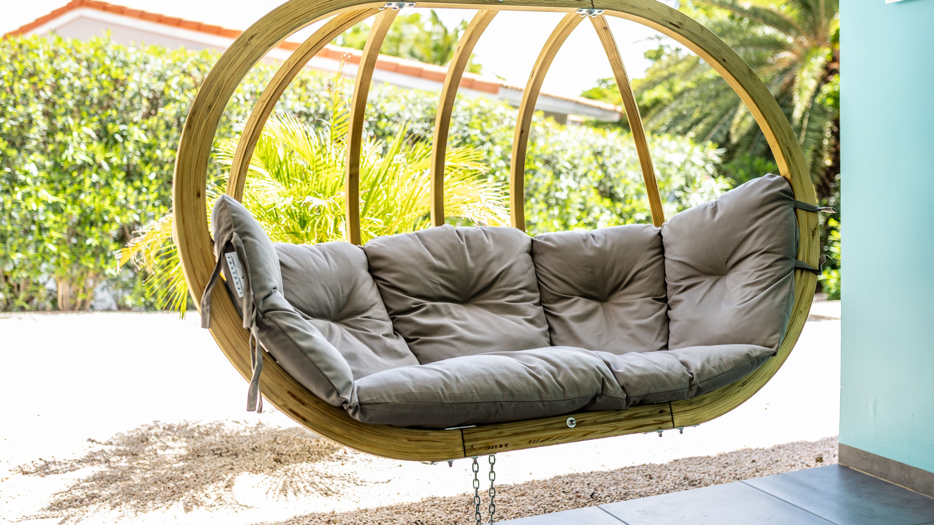 A wicker swing chair with grey cushions in a garden setting.