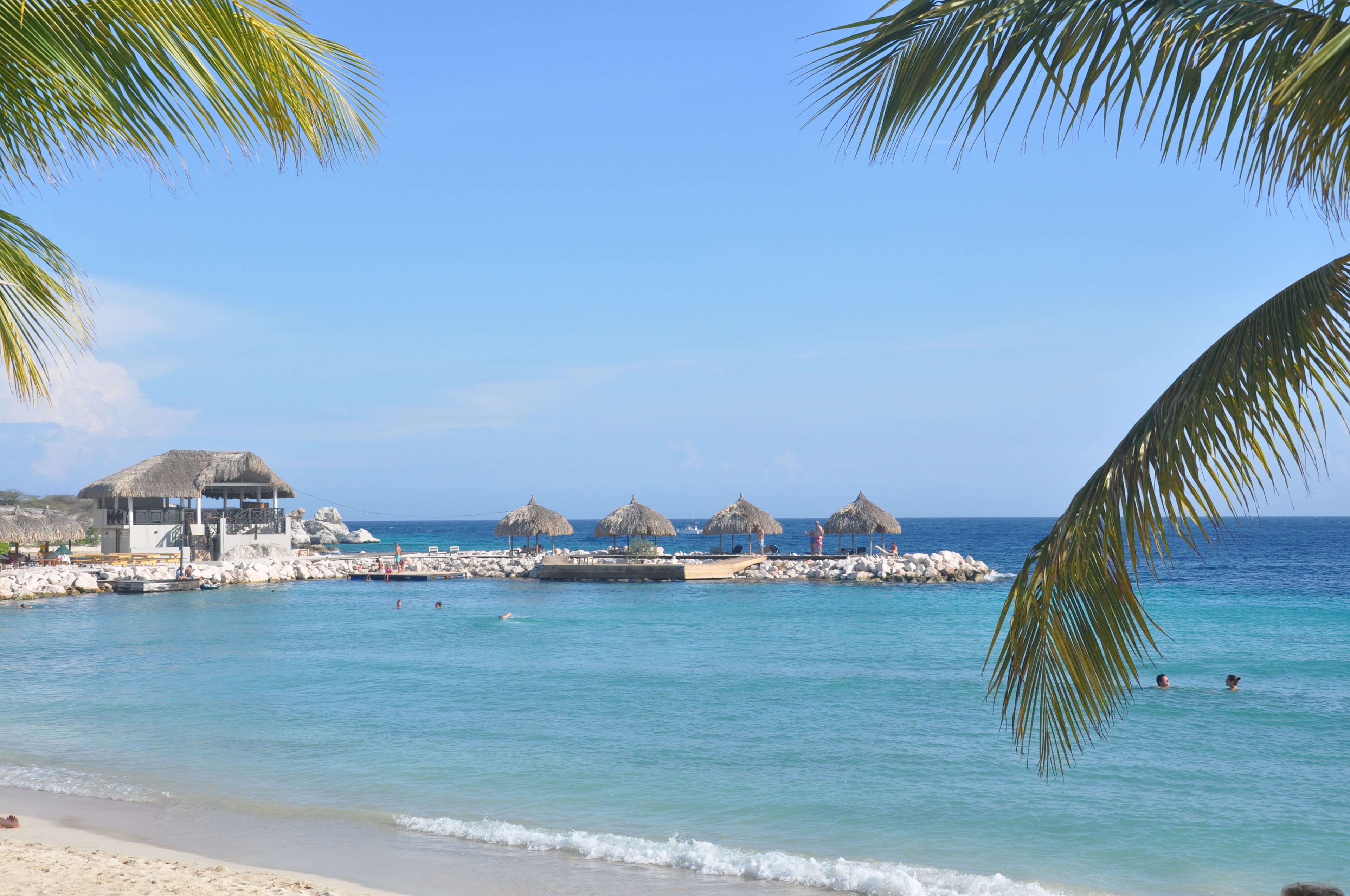 A beach with thatched-roof structures, a rocky shoreline, and clear blue water.