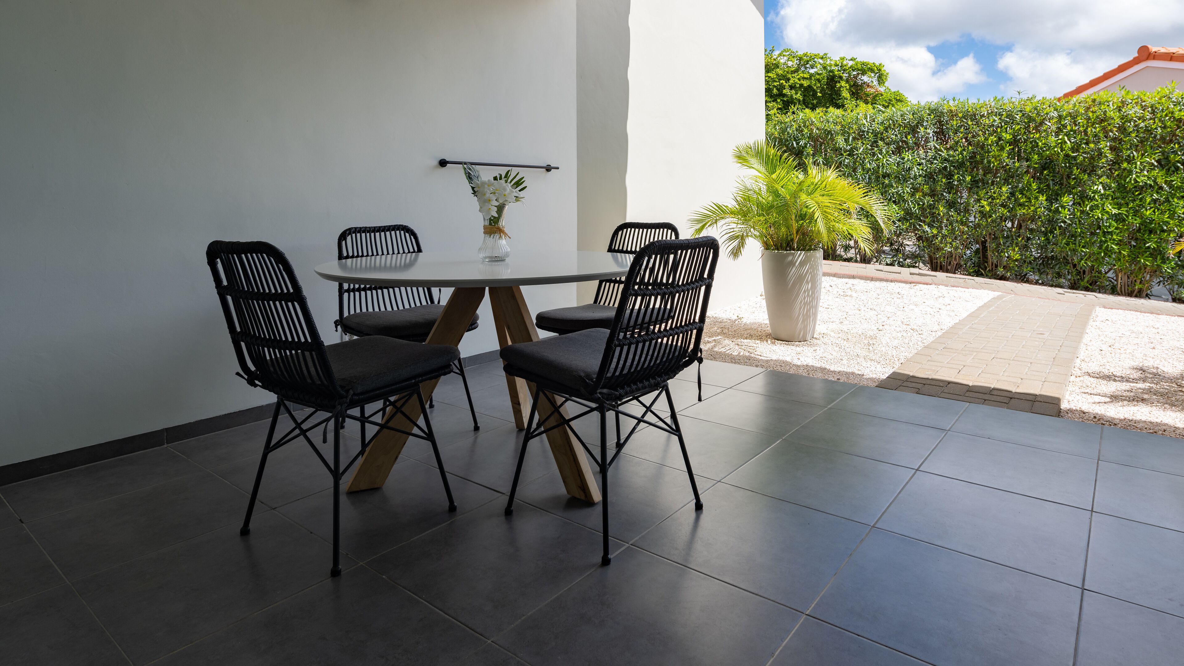 Un coin repas avec une table ronde et quatre chaises noires, un vase avec des fleurs et une plante en pot.
