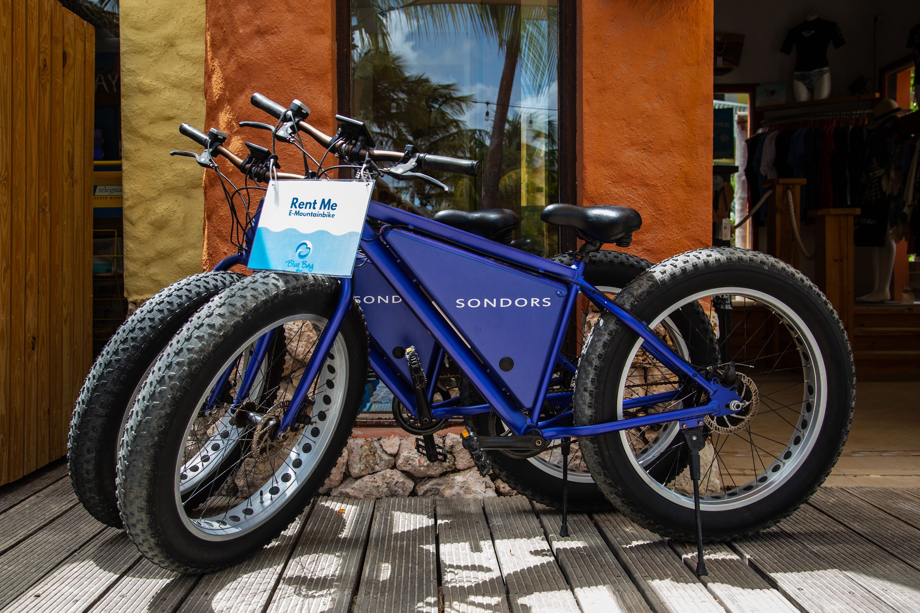 A blue bicycle with a sign that reads "Rent Me" parked on a wooden deck.