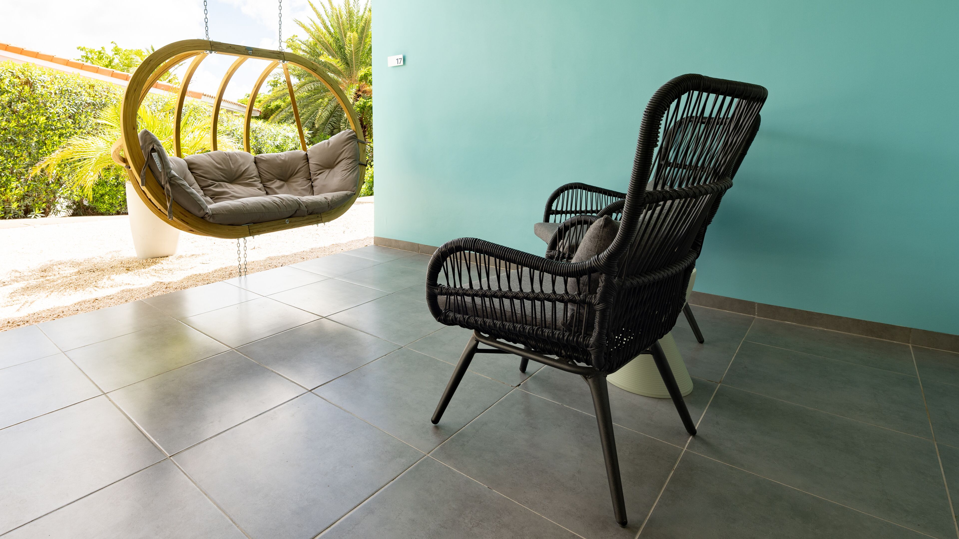 A room with a hanging chair, a wicker chair, and a tiled floor.