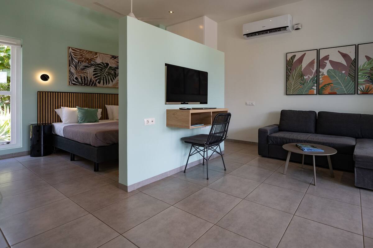 A modern living room with a sofa, a chair, a TV mounted on the wall, and a bed with a headboard.