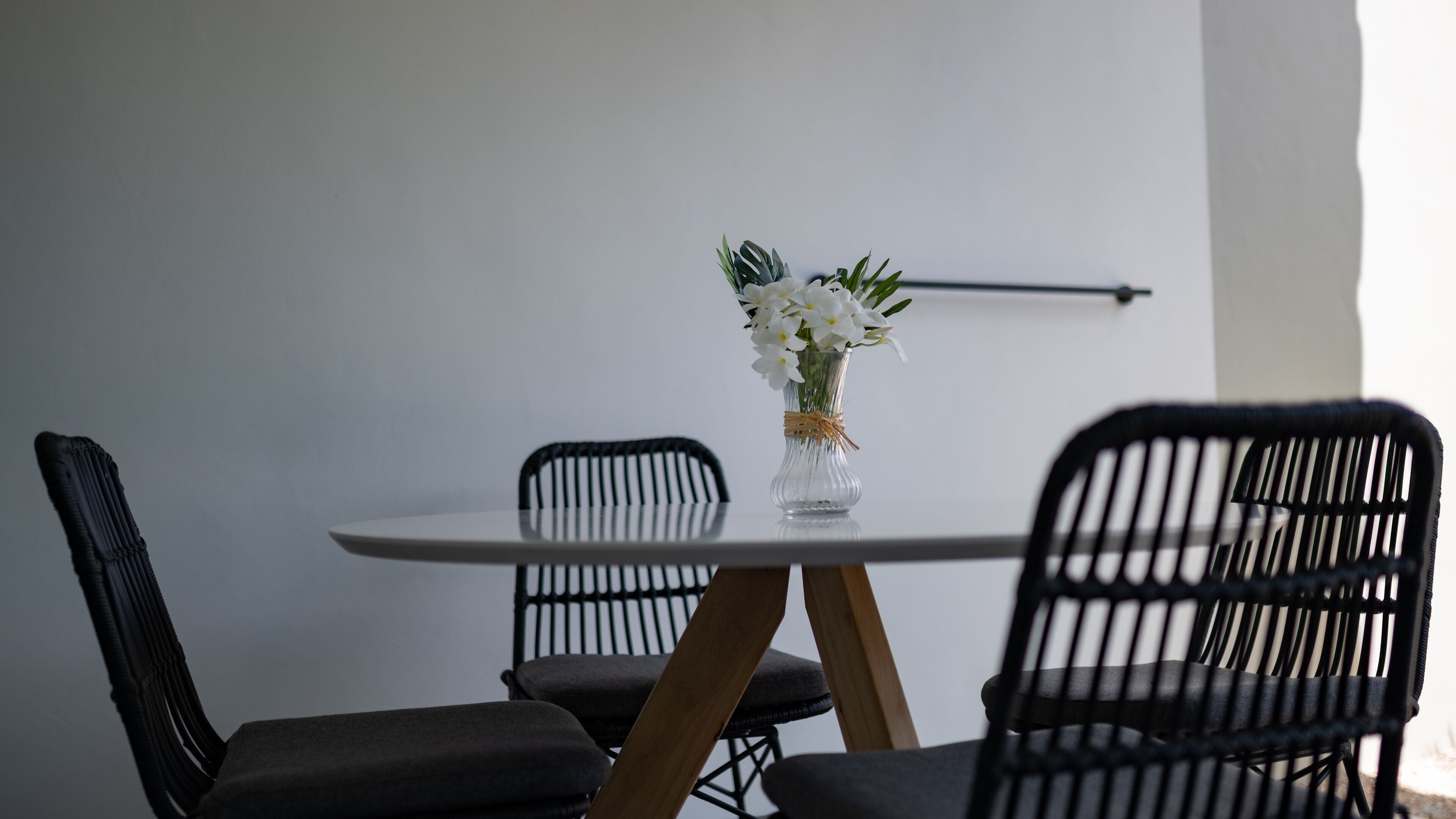 Una mesa de comedor con un jarrón de flores blancas, rodeada de sillas negras con patas de madera.