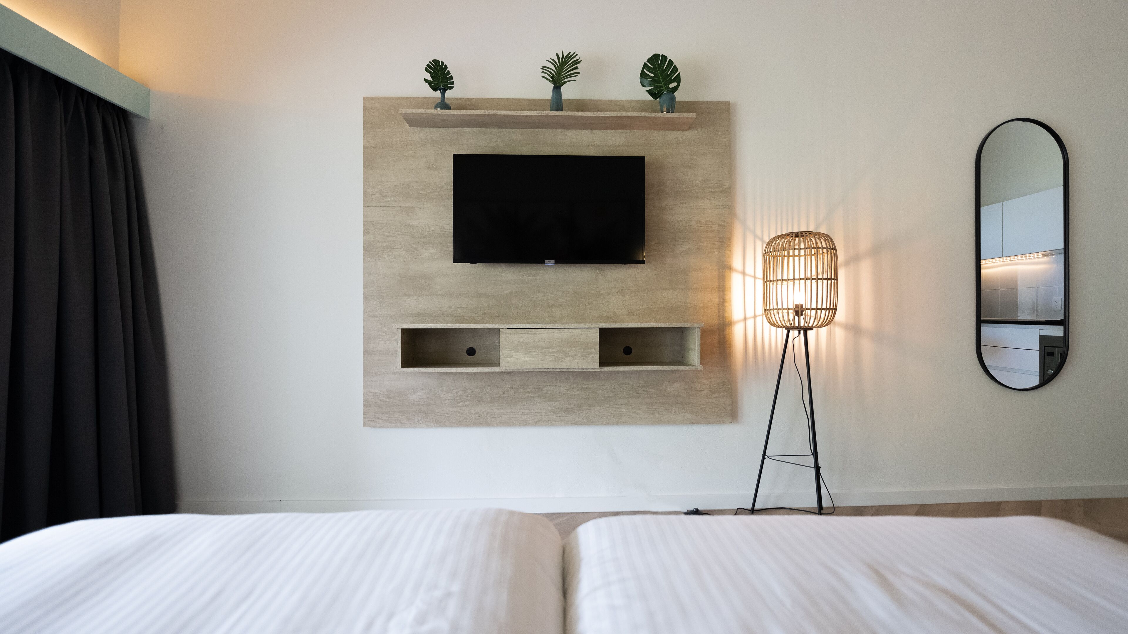 A hotel room with a mounted TV, a bedside lamp, and a mirror on the wall.