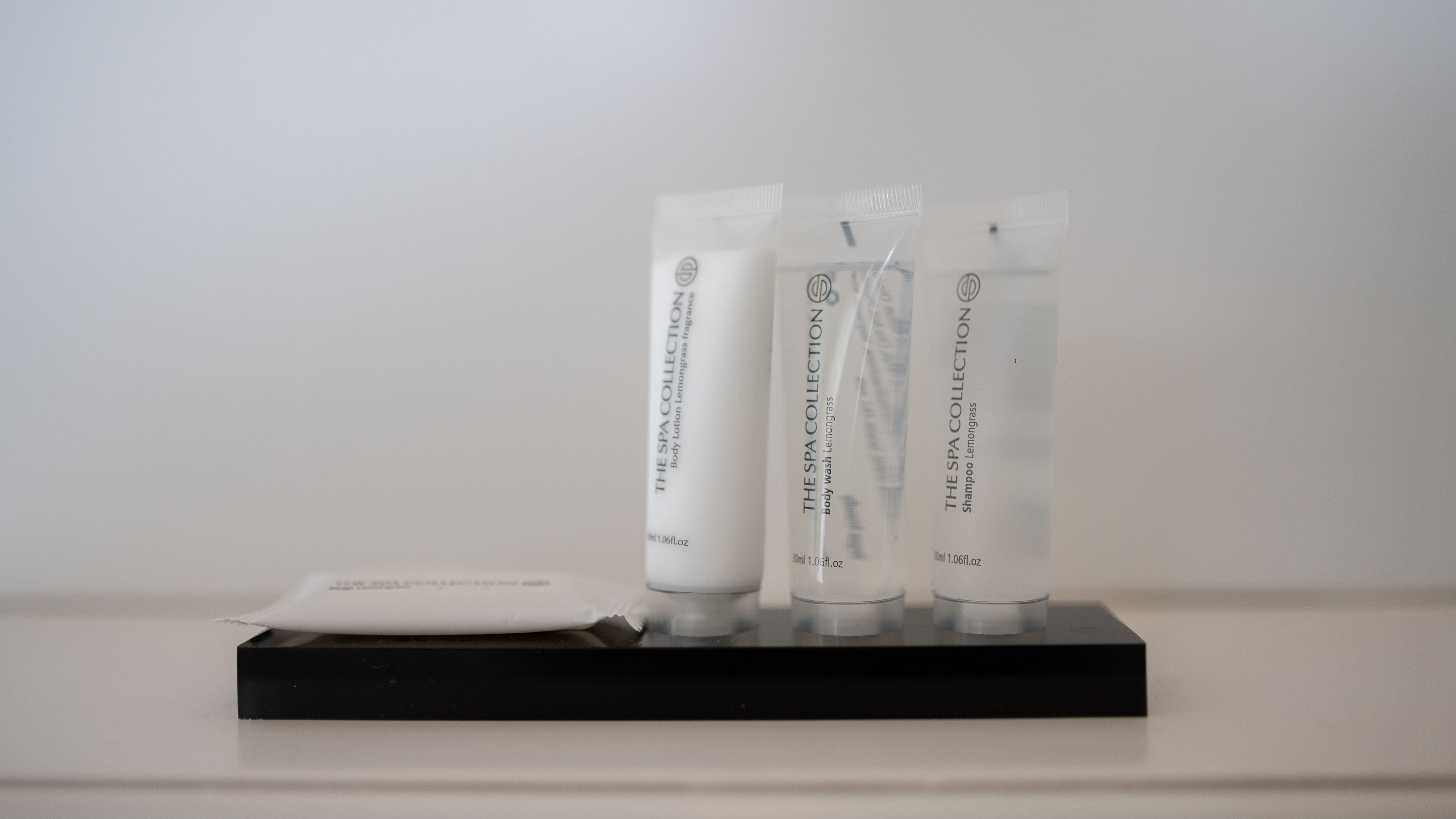 Three spa collection body wash tubes and a sachet on a black stand against a white background.