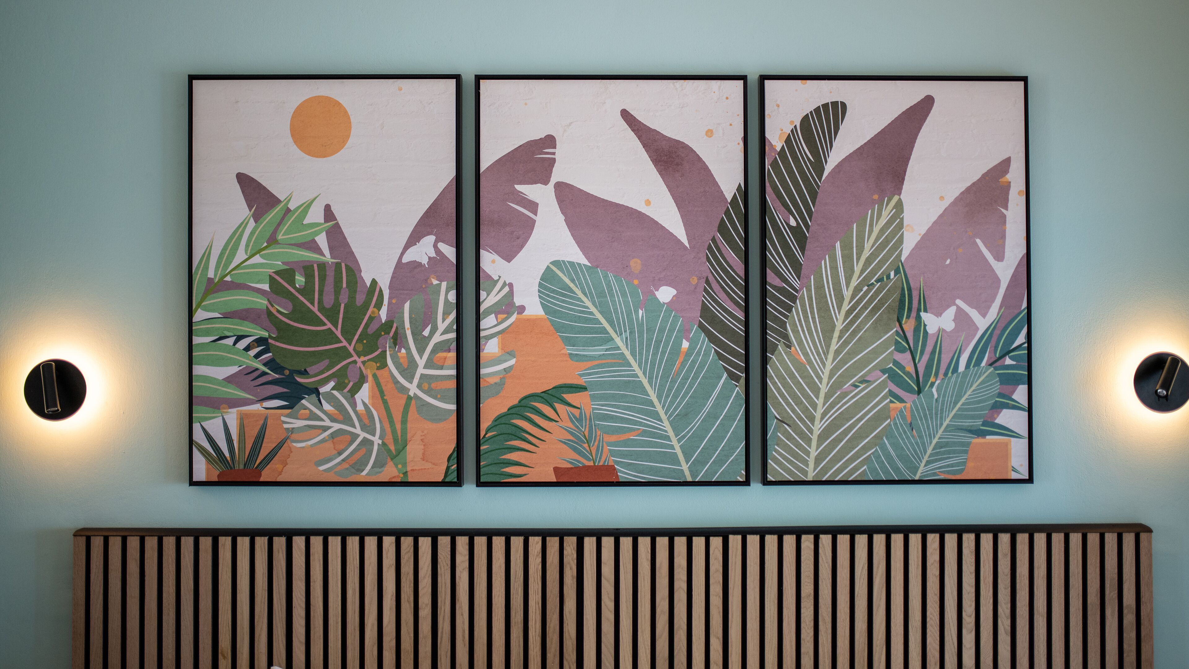 A wall-mounted triptych artwork with tropical foliage and a sun.