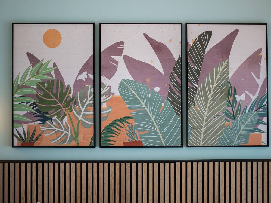 A wall-mounted triptych artwork with tropical foliage and a sun.