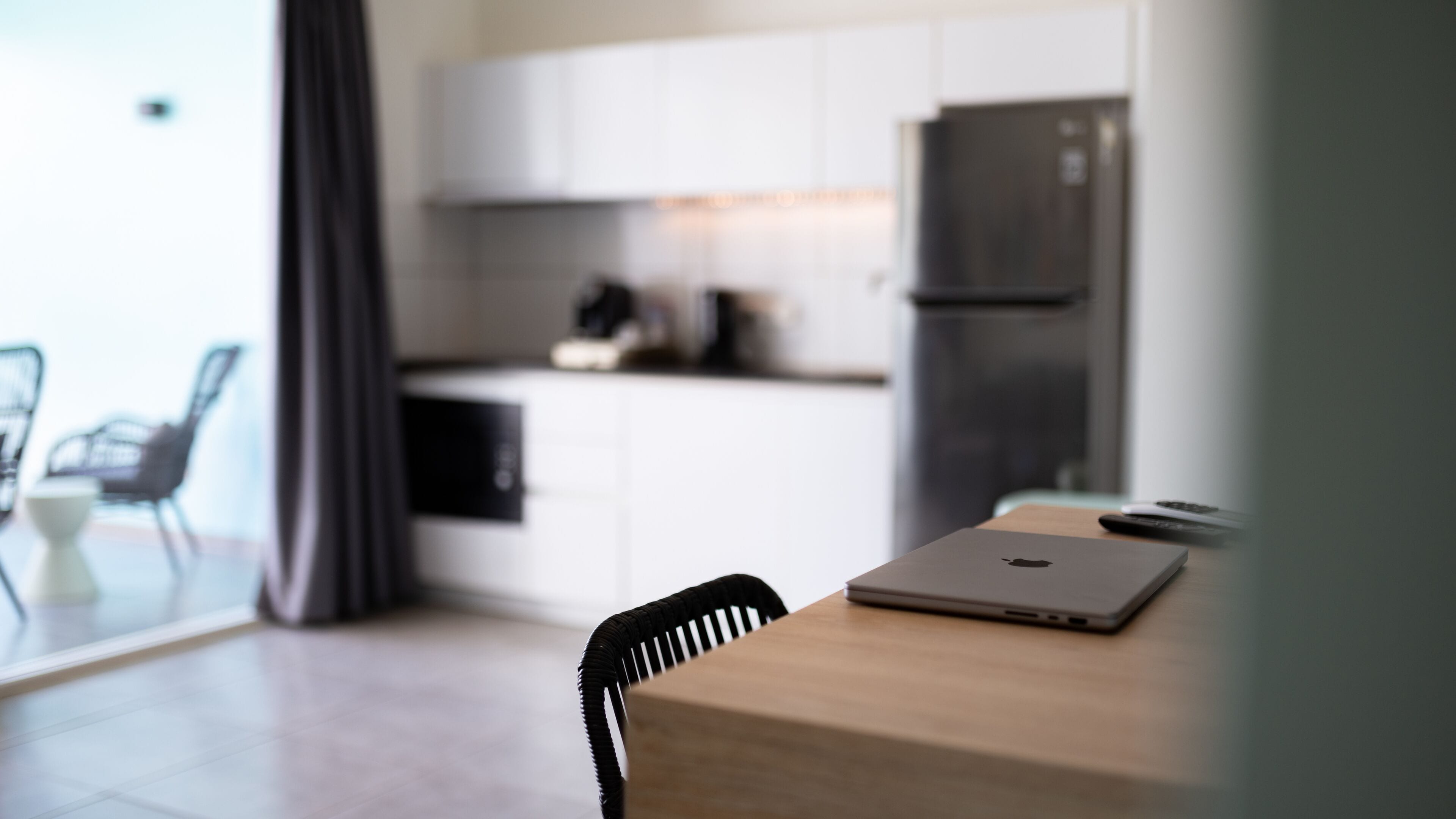 A modern kitchen with white cabinets, a black refrigerator, and a laptop on a wooden table.