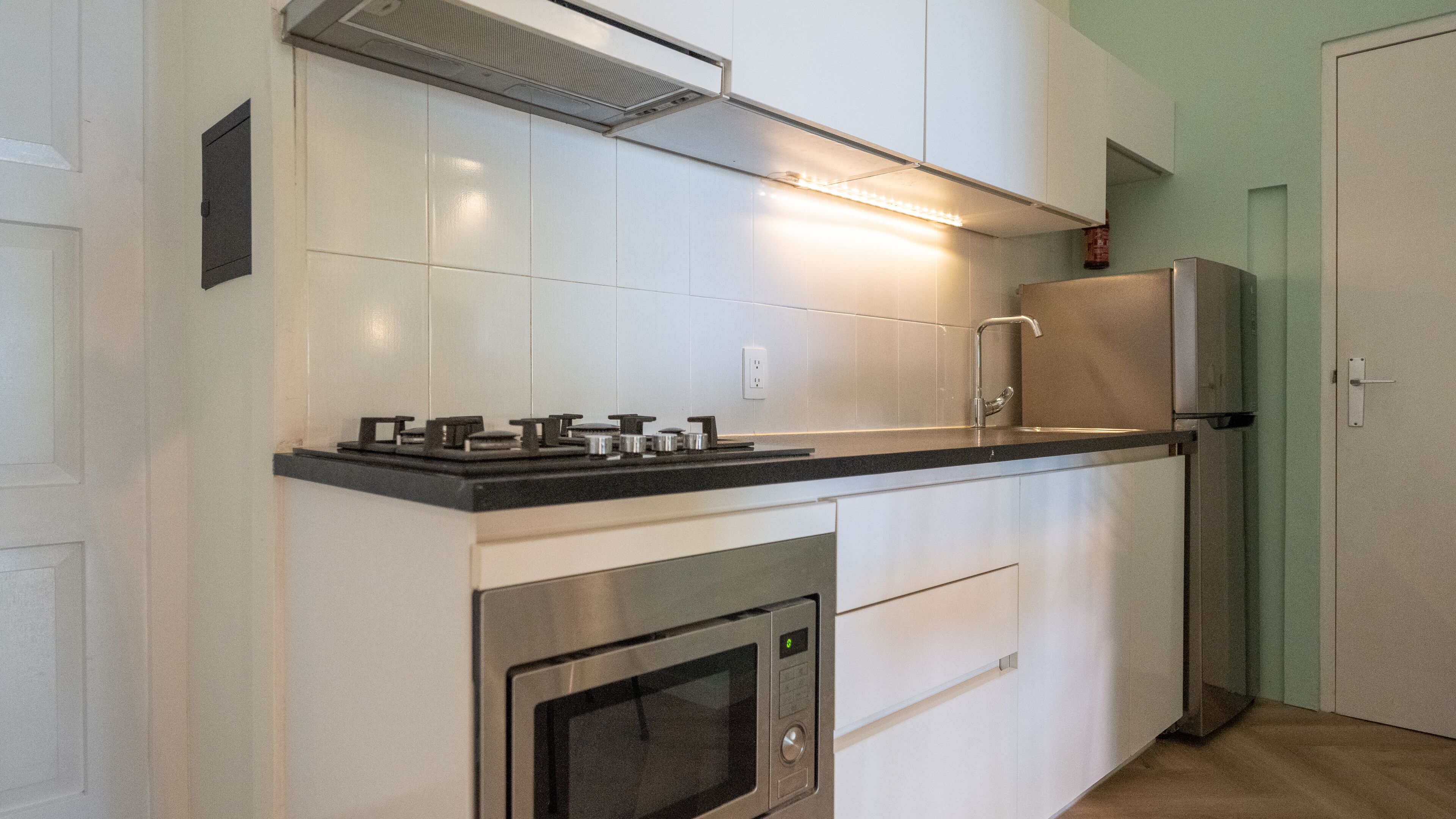 Una cuina moderna amb armaris blancs, un frigorífic d'acer inoxidable, un forn de sobre i una placa de gas.