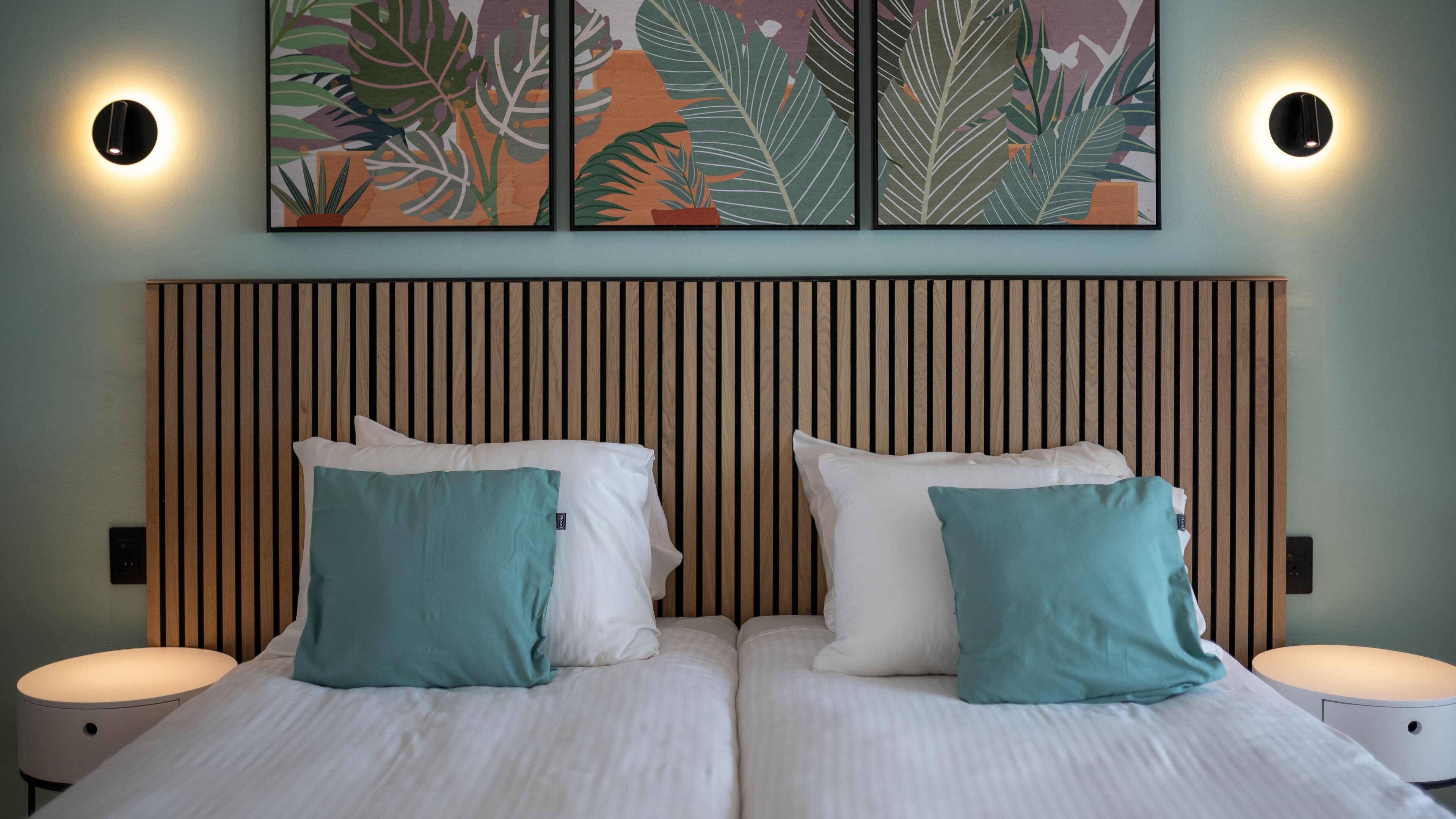 Una cama doble con dos almohadas, cabecera de listones de madera y dos lámparas de pared.