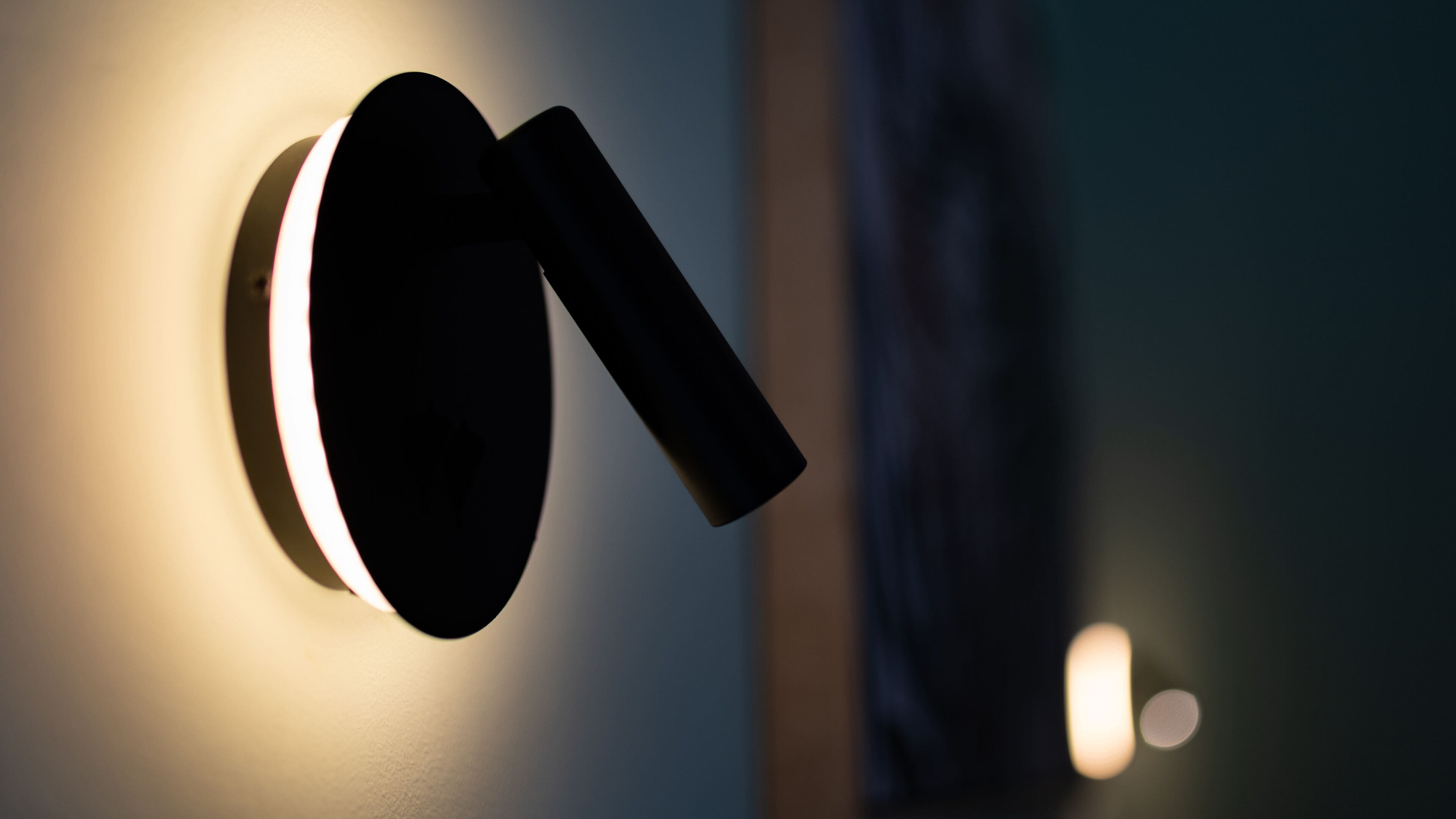 A modern wall-mounted light fixture with a circular base and a vertical arm.