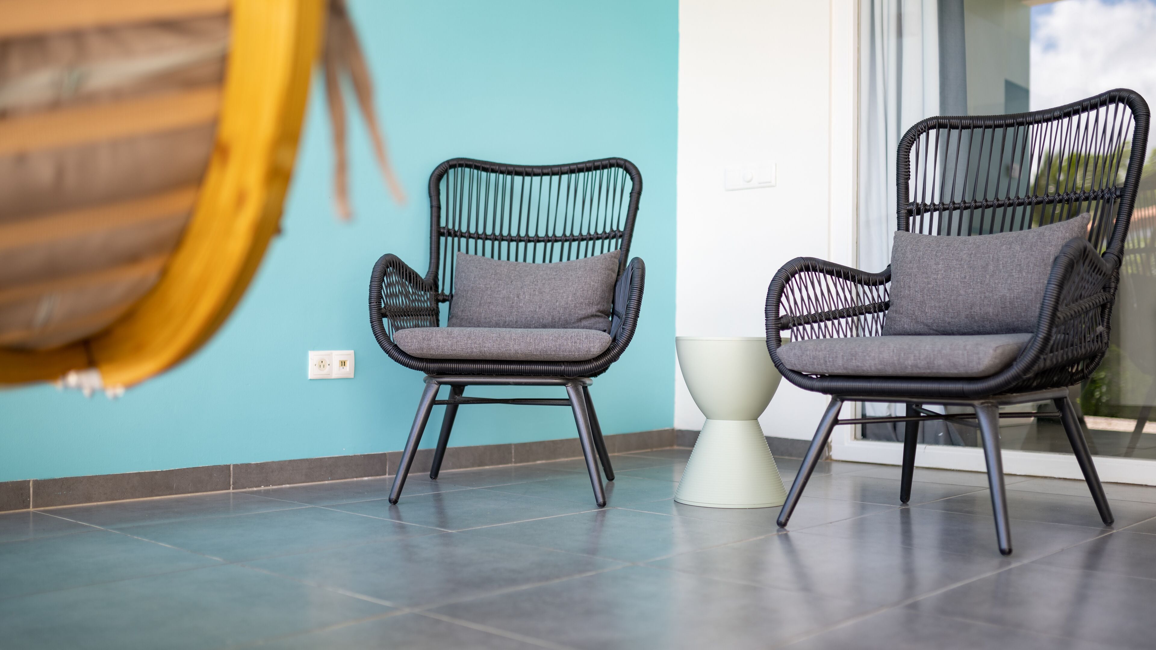 Two black wicker chairs with grey cushions in a room with teal walls and a tiled floor.