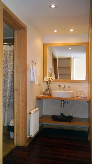 A bathroom with a wooden vanity, a large mirror, a white sink, and a shower area with a floral curtain.