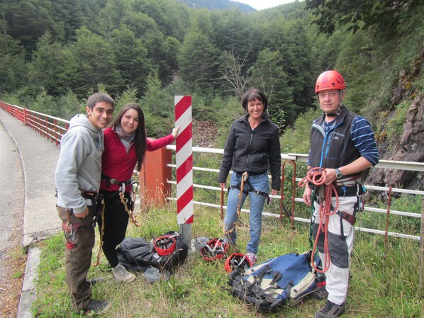 A group of people with climbing gear near a red and white striped sign, standing on a grassy area beside a road with a forested hillside in the background.