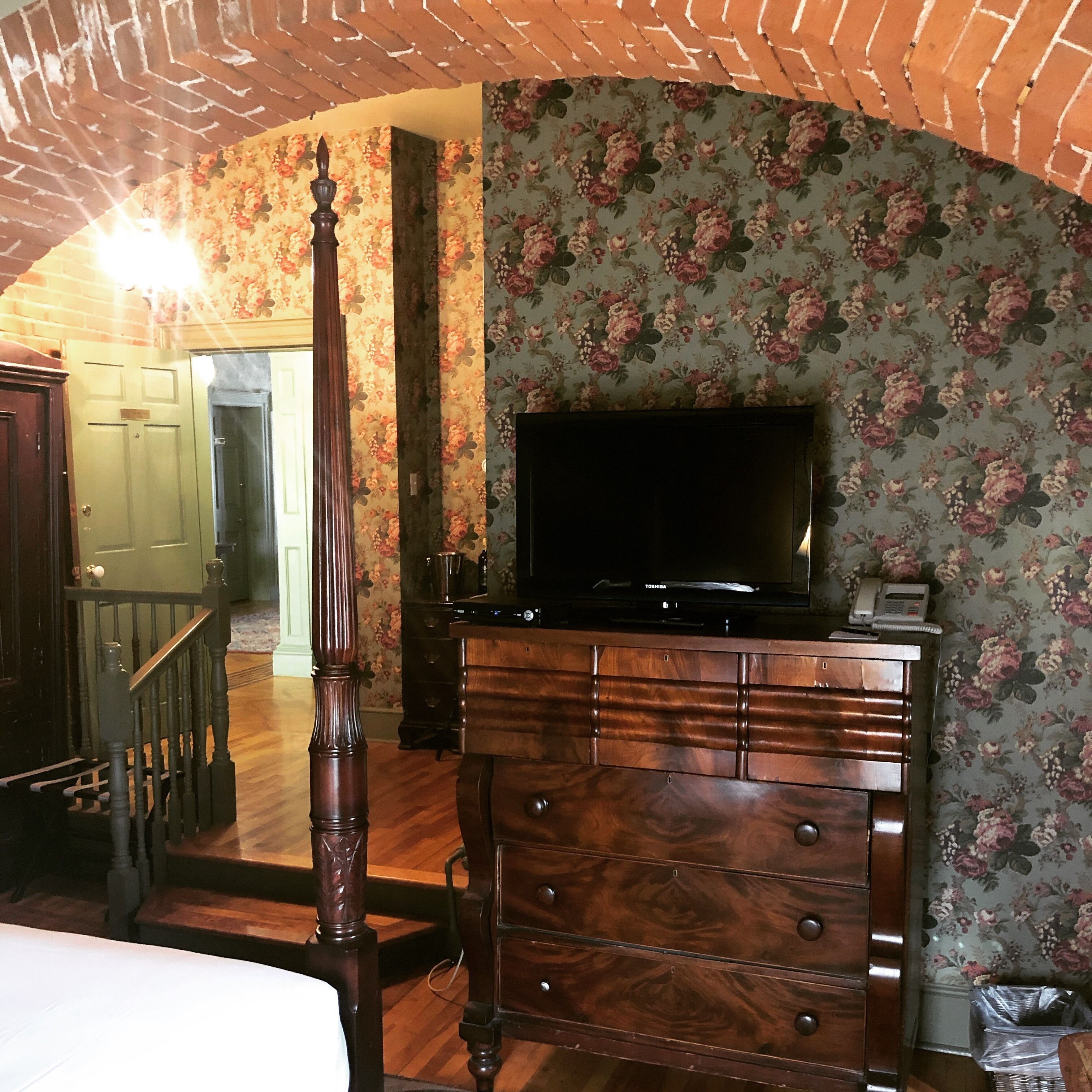 Un dormitorio con un aparador de madera, un televisor encima y papel tapiz floral.