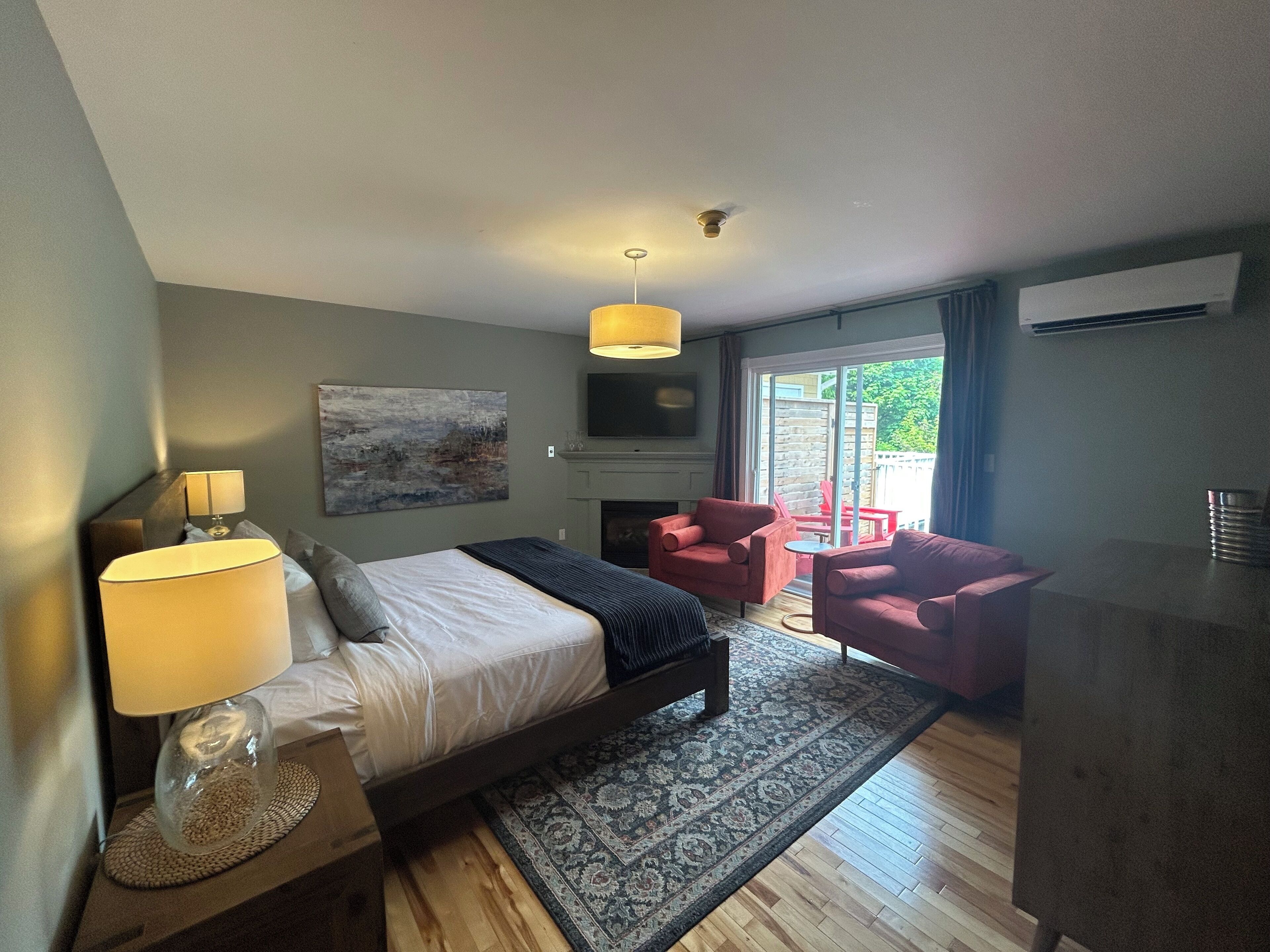 A bedroom with a bed, bedside lamps, a fireplace, a TV, and a view of the outside.