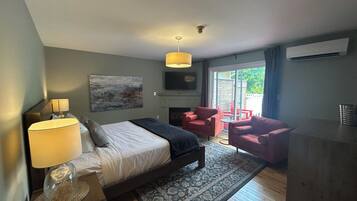 A bedroom with a bed, bedside lamps, a fireplace, a TV, and a view of the outside.