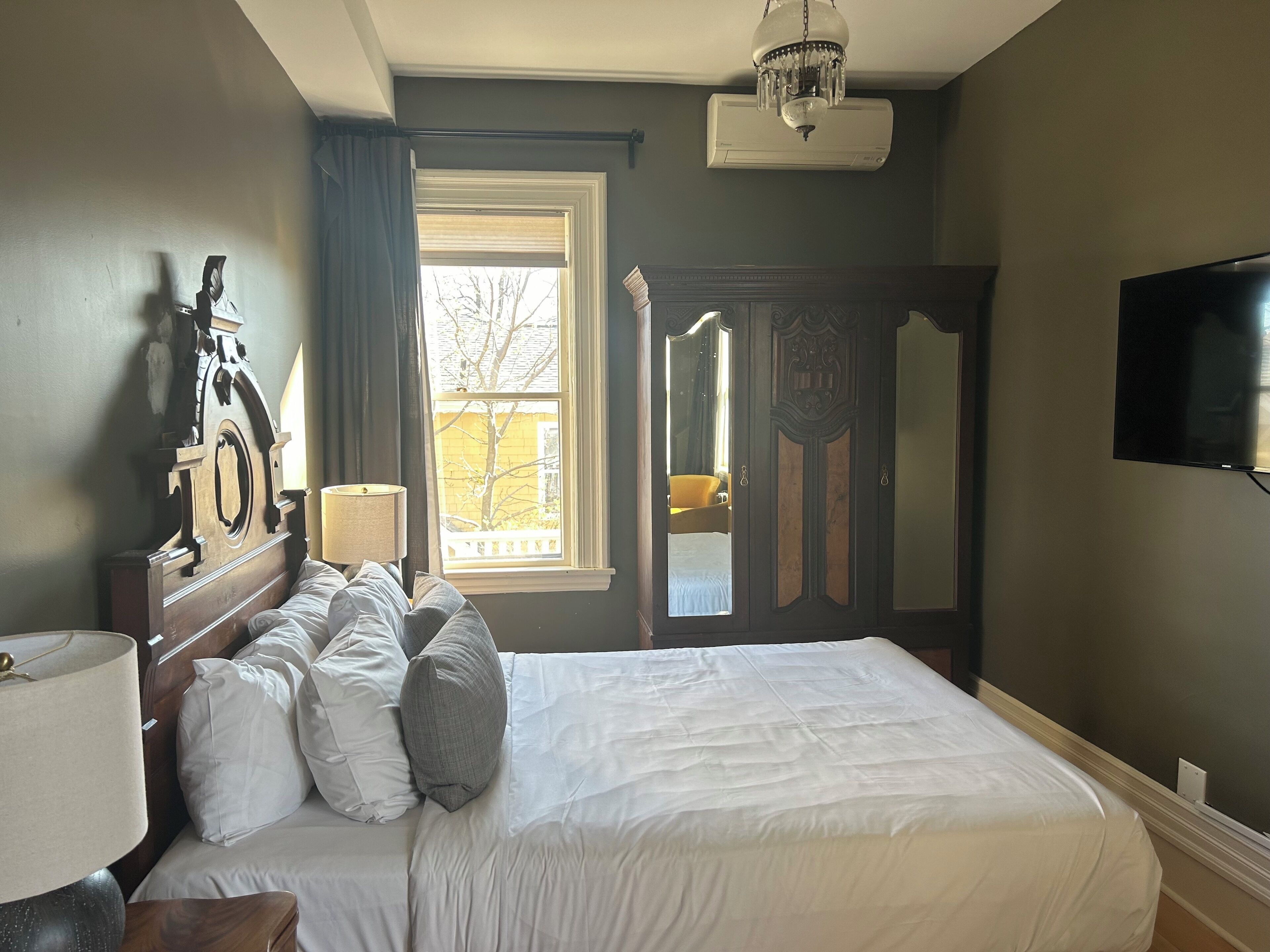 Een slaapkamer met een groot bed, een nachtkastje, een lamp, een spiegel, een kledingkast en een televisie.