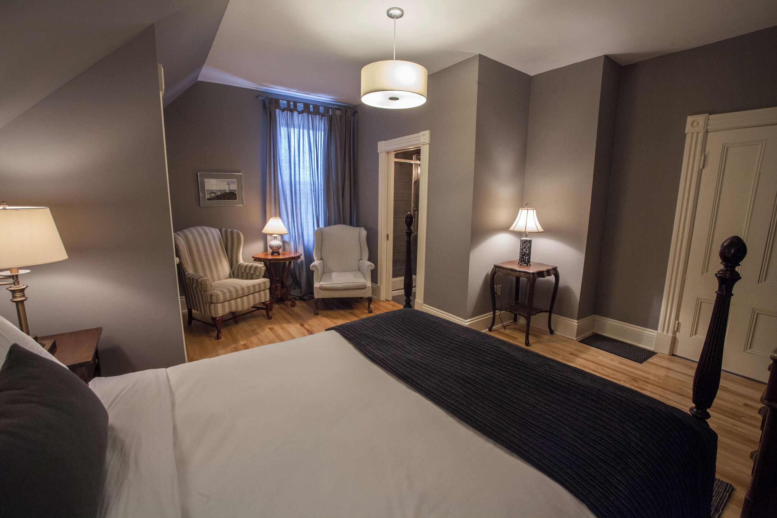 A hotel room with a large bed, two armchairs, a small table, a lamp, and a door.