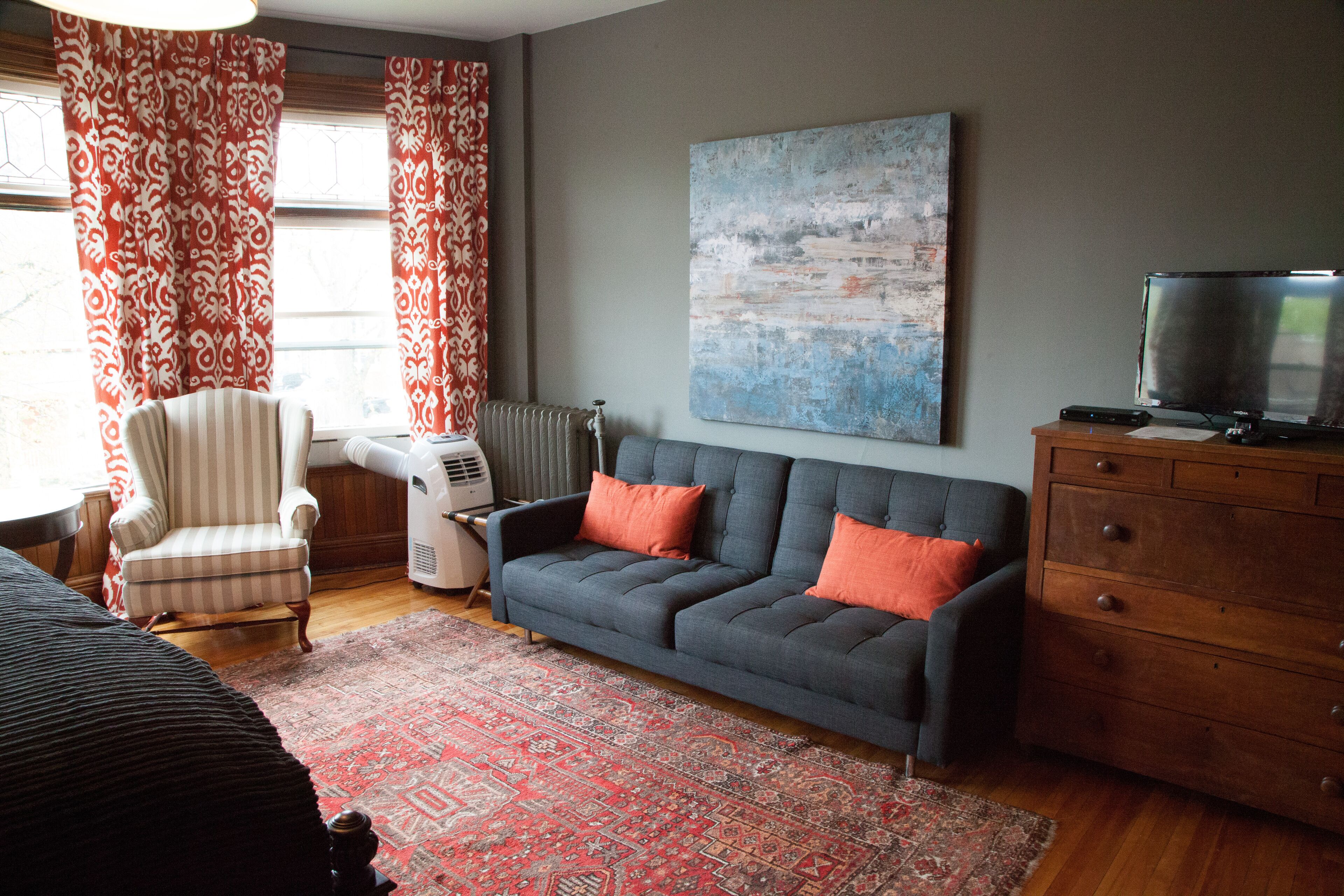 A living room with a grey sofa, striped armchair, and a red patterned rug.
