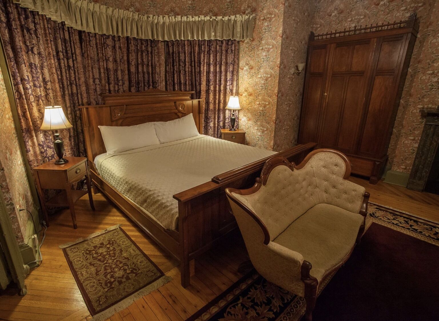Un dormitorio tradicional con una cama de madera, dos lámparas de noche, una silla y un armario.