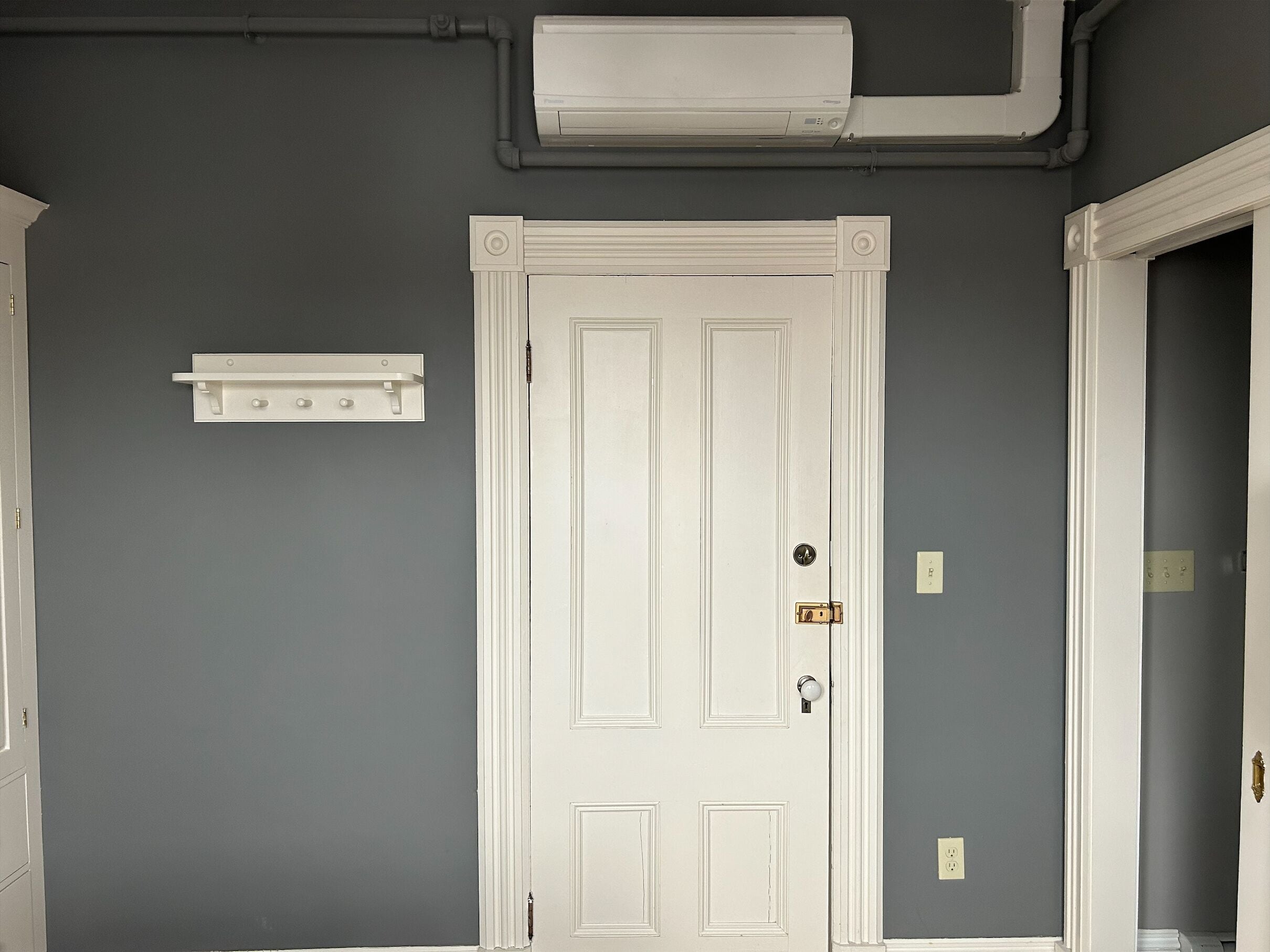 A room with a white door, a white wall-mounted shelf, and a grey wall.