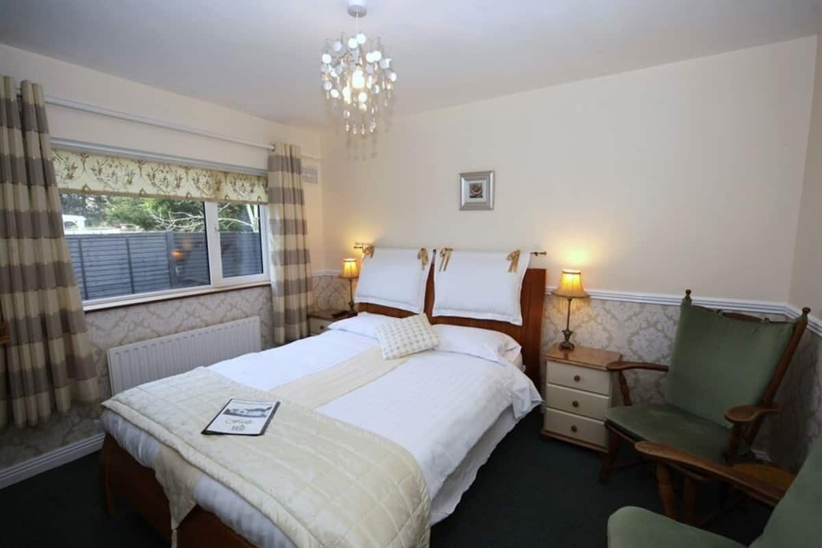 A hotel room with a double bed, bedside lamps, a chair, a nightstand, and a window with curtains.