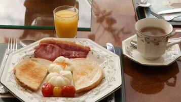 A breakfast plate with toast, bacon, eggs, and tomatoes on a floral-patterned plate, a glass of orange juice, and a cup of coffee on a table.