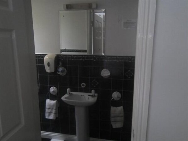 Un baño con un lavabo blanco, paredes cubiertas de azulejos negros y un espejo sobre el lavabo.