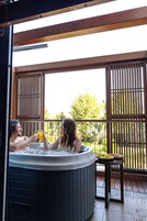 Un jacuzzi con dos personas adentro, rodeado de barandillas de madera y vistas a follaje.