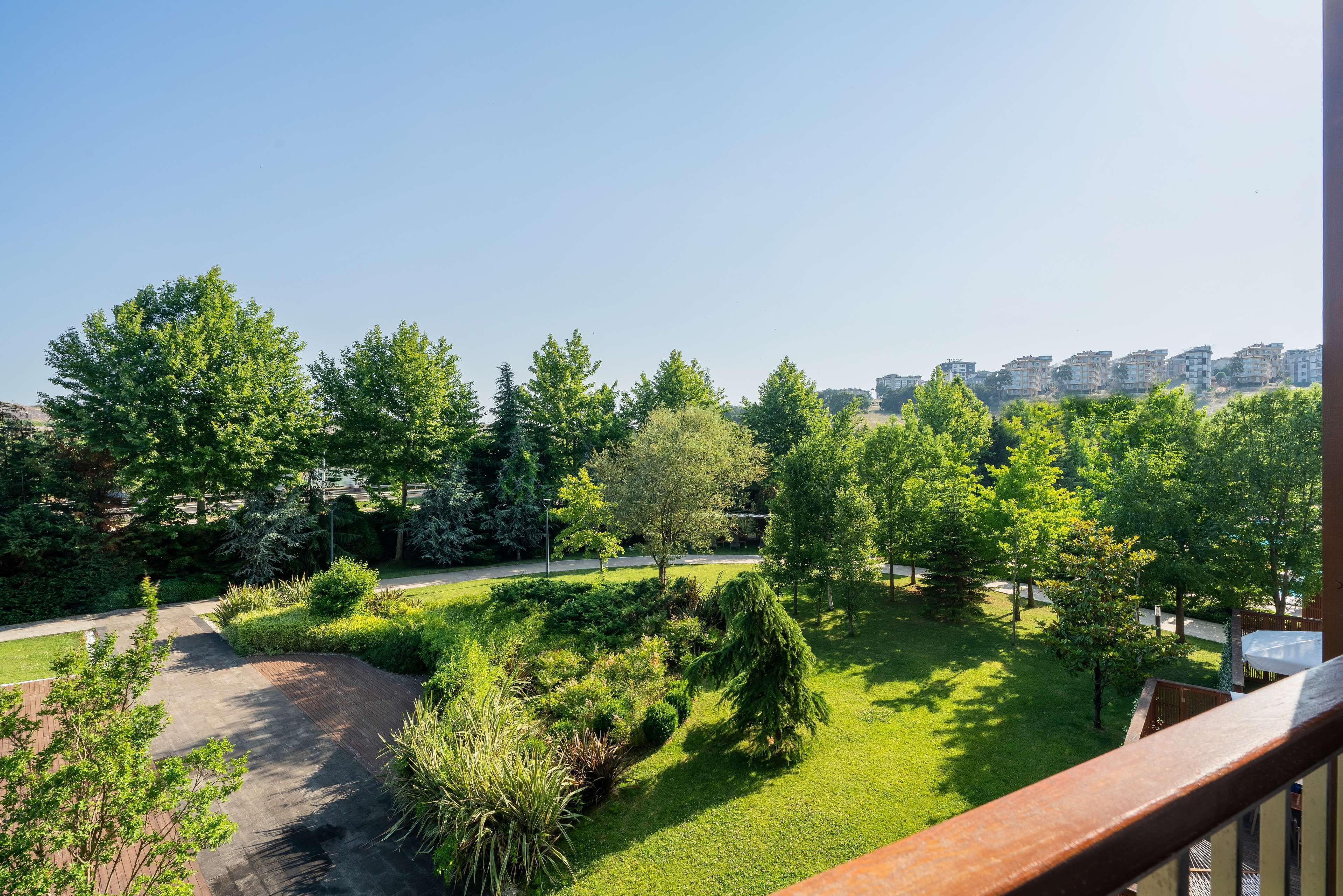 A balcony with a view of a well-maintained garden and a distant cityscape.