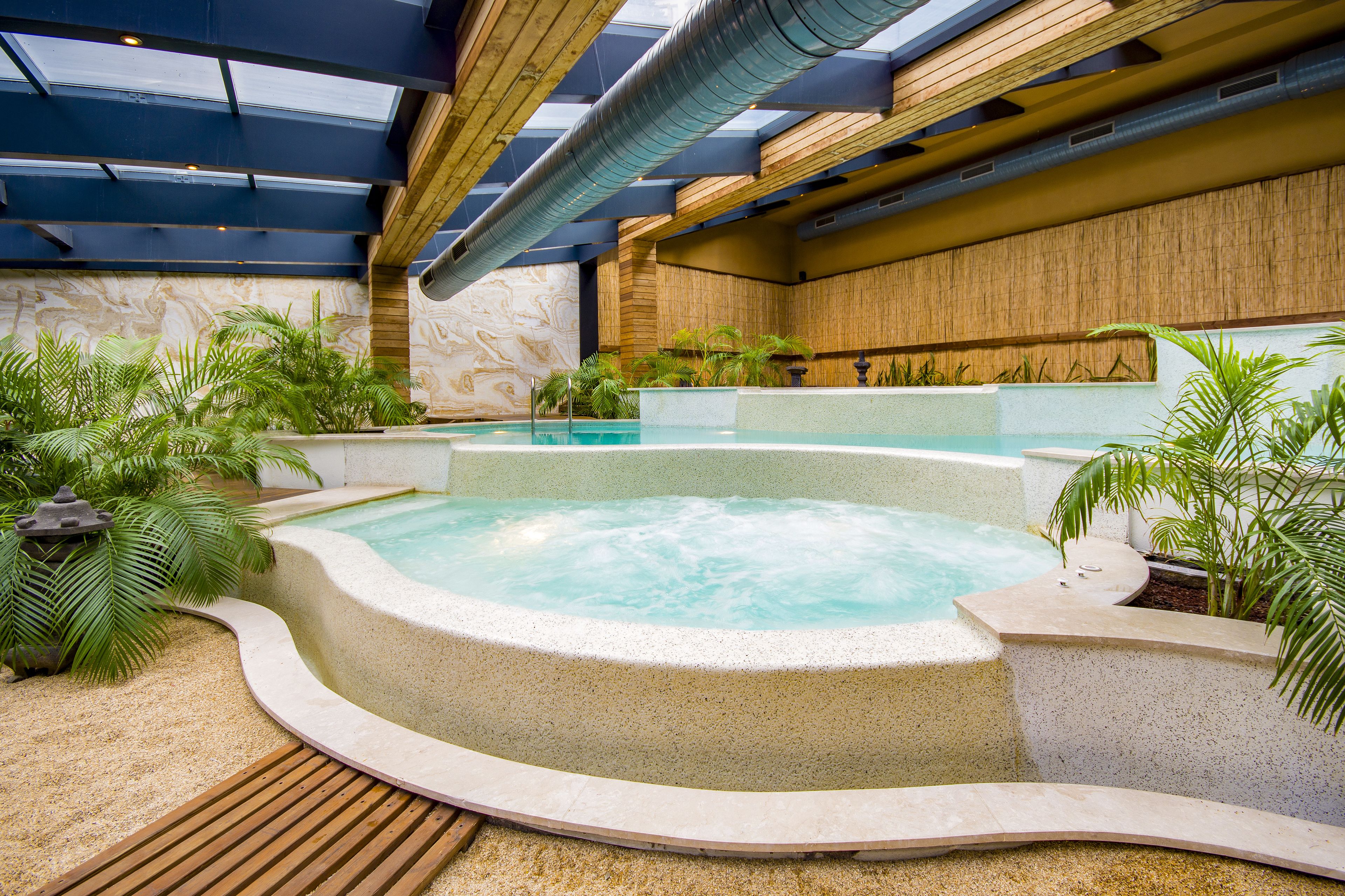 A hot tub area with a wooden deck, surrounded by plants and a stone wall.