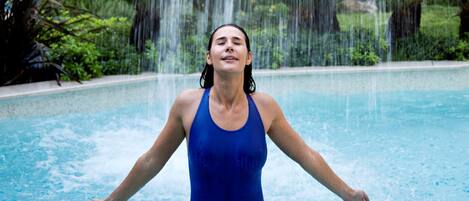 Una persona in costume blu in piscina con getti d'acqua.