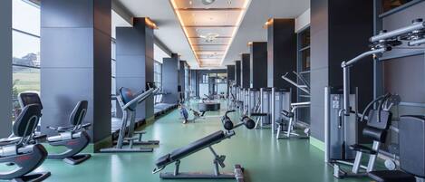 A gym with various exercise equipment, large windows, and a modern ceiling design.