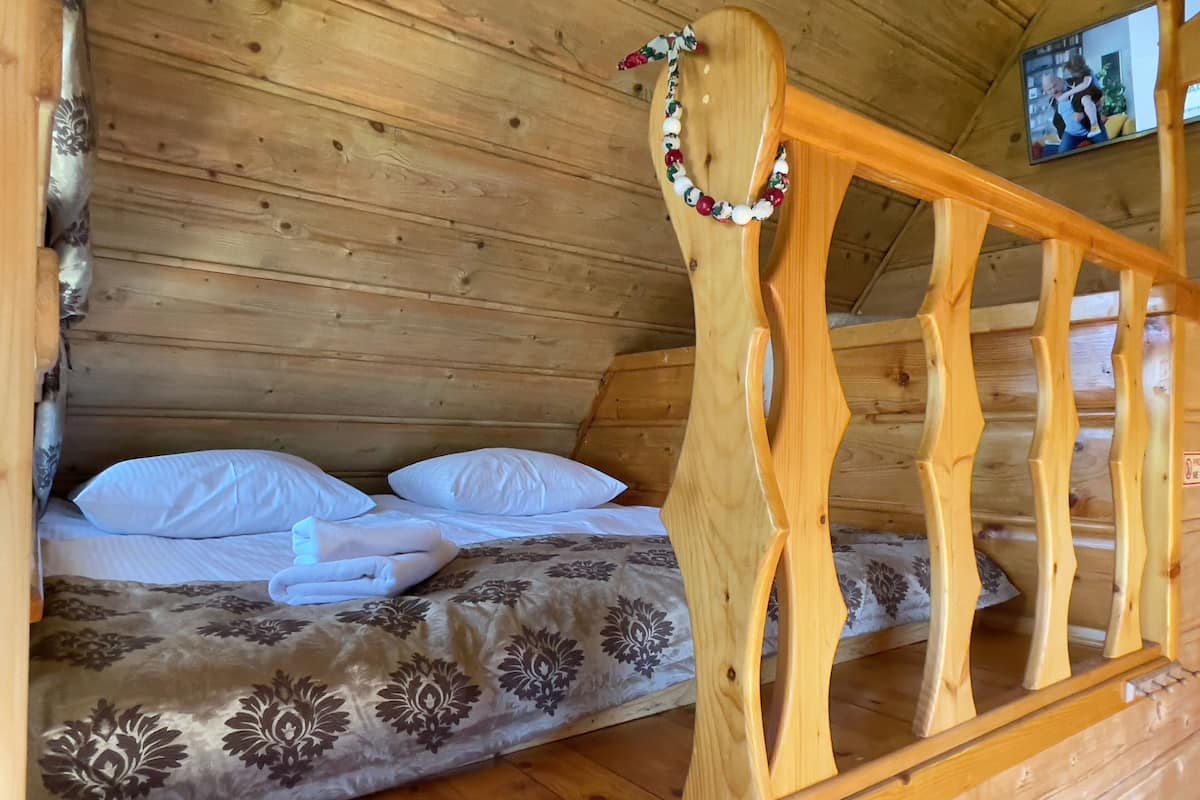 Ein Zimmer in einer Holzhütte mit einem Bett, Kissen, einer Decke und einem Holz-Kopfteil.