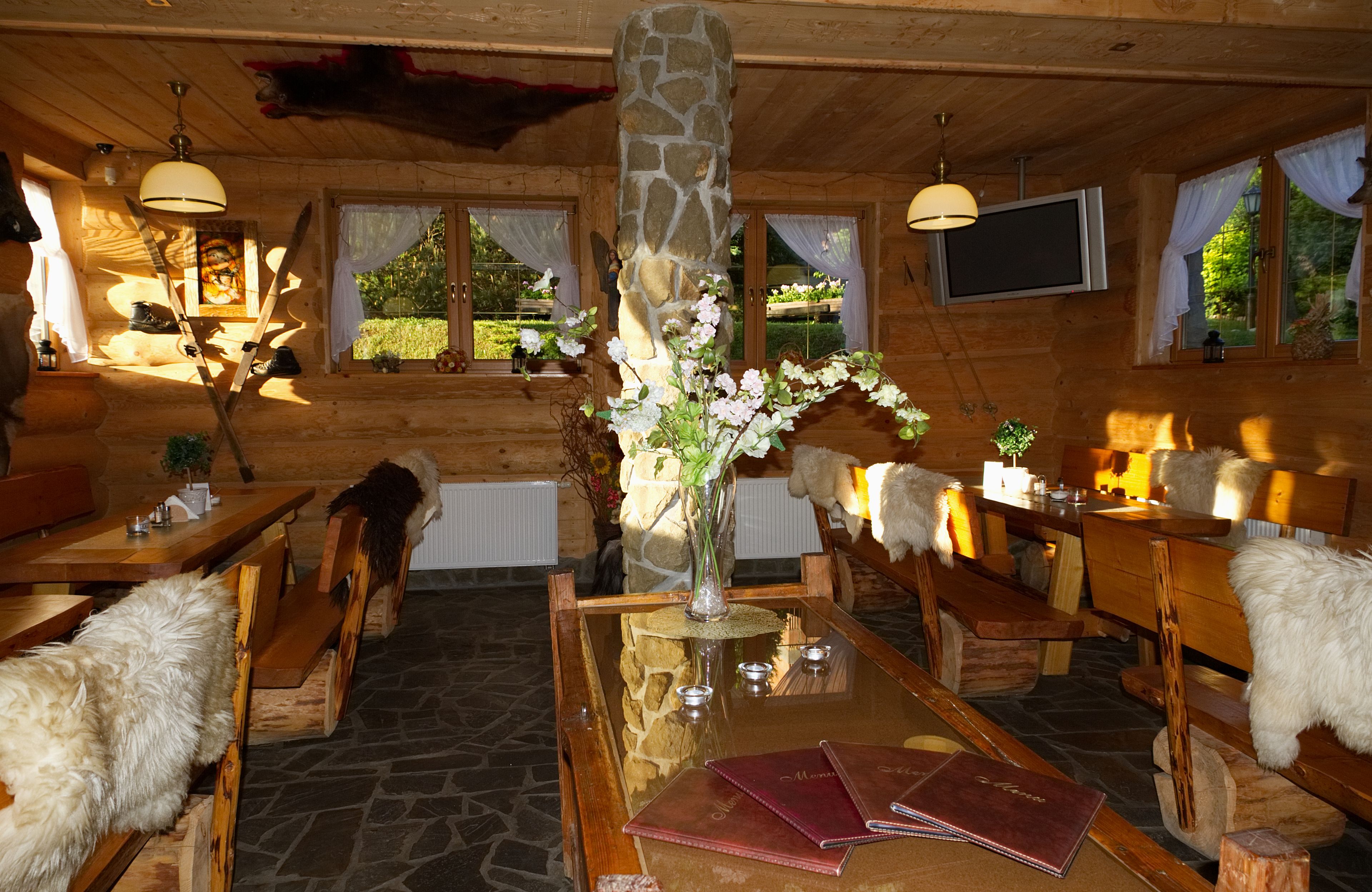 A wooden cabin interior with stone pillars, wooden benches, a dining table, and a fireplace.