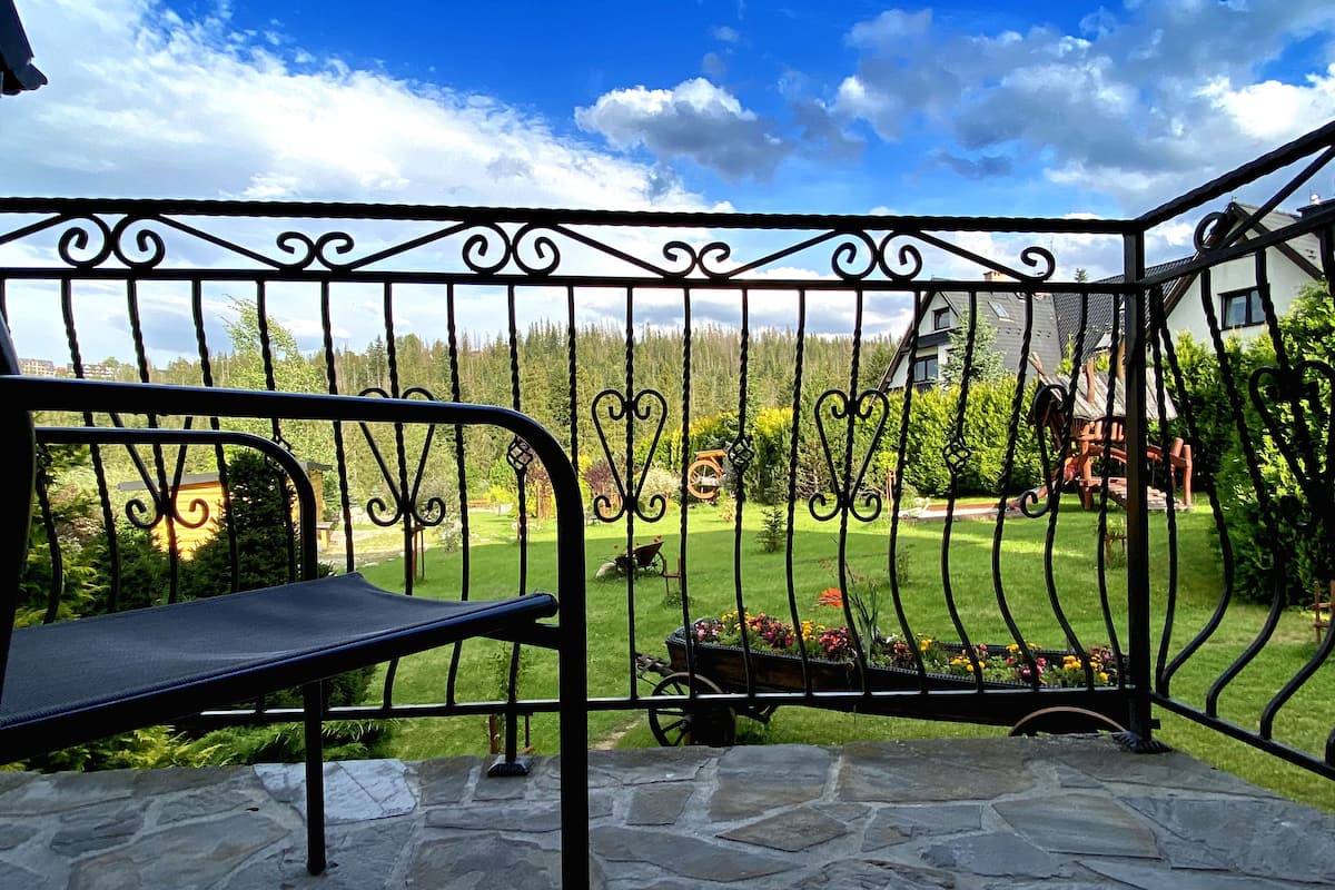 Eine terrasse aus Naturstein mit Metallgeländer, einer Bank und Blick auf einen gepflegten Rasen und Bäume.