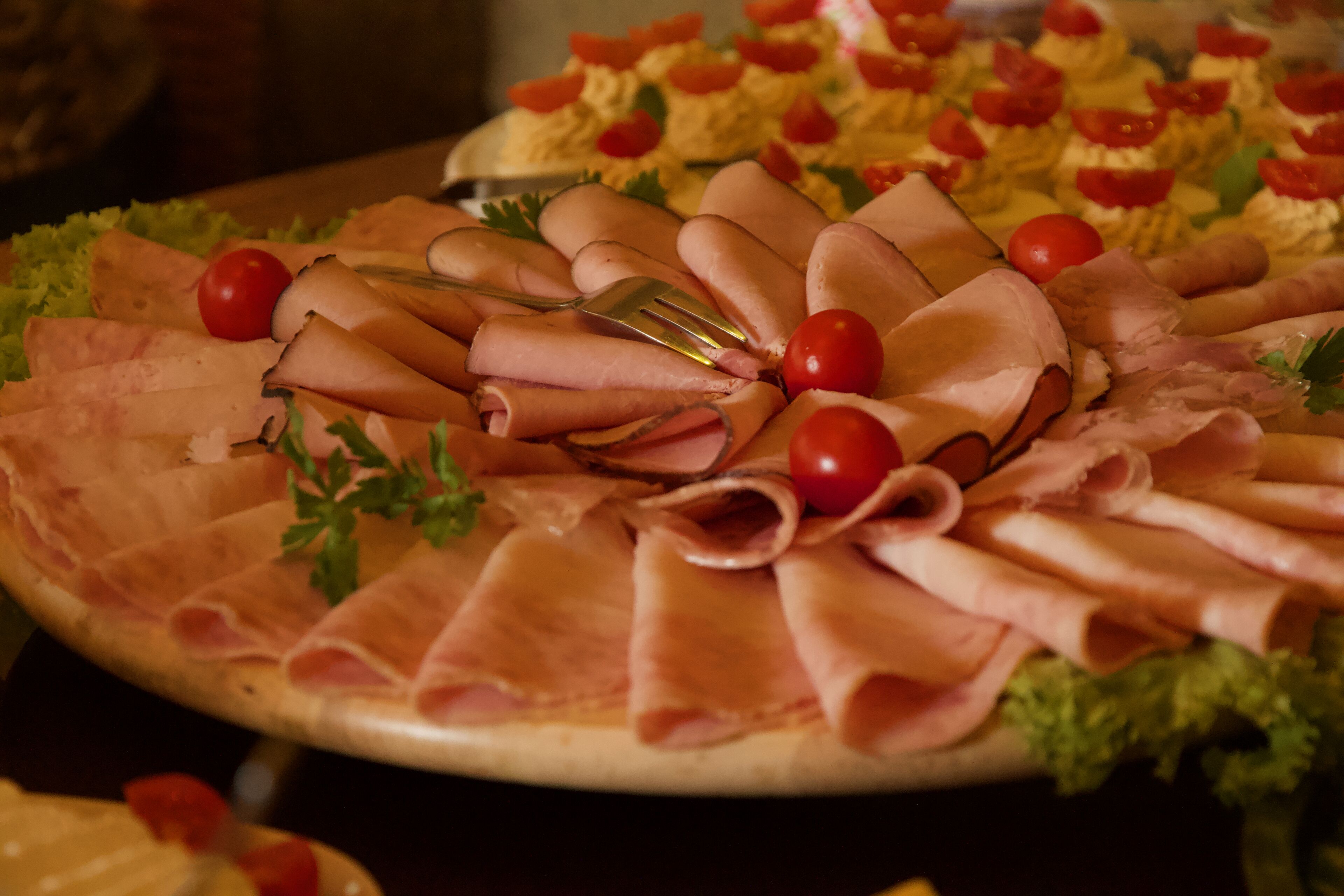 A platter of sliced meats and tomatoes on a wooden board.