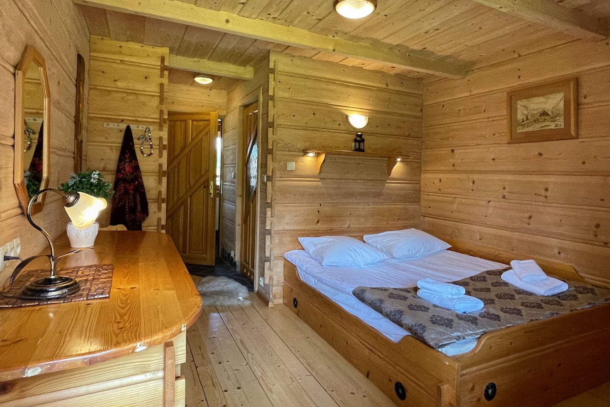 Ein Zimmer einer Holzhütte mit einem Bett, einem Schreibtisch mit Lampe und einem Spiegel.
