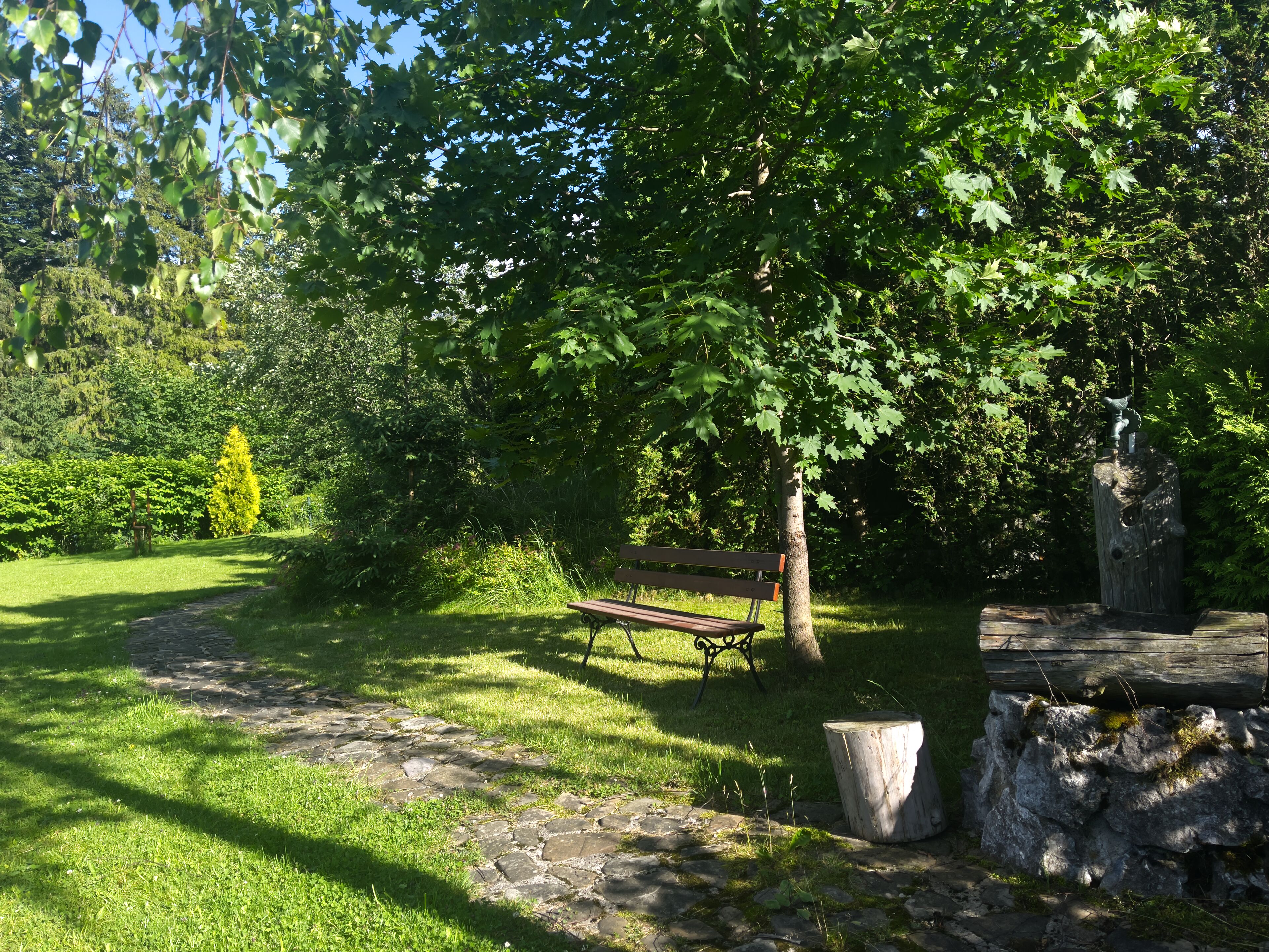 A park with a stone path, a wooden bench, and a rustic wooden structure.