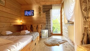 A cozy log cabin room with two beds, a television, a radiator, and a large window with curtains. - Pensjonat u Ani (Zakopane)
